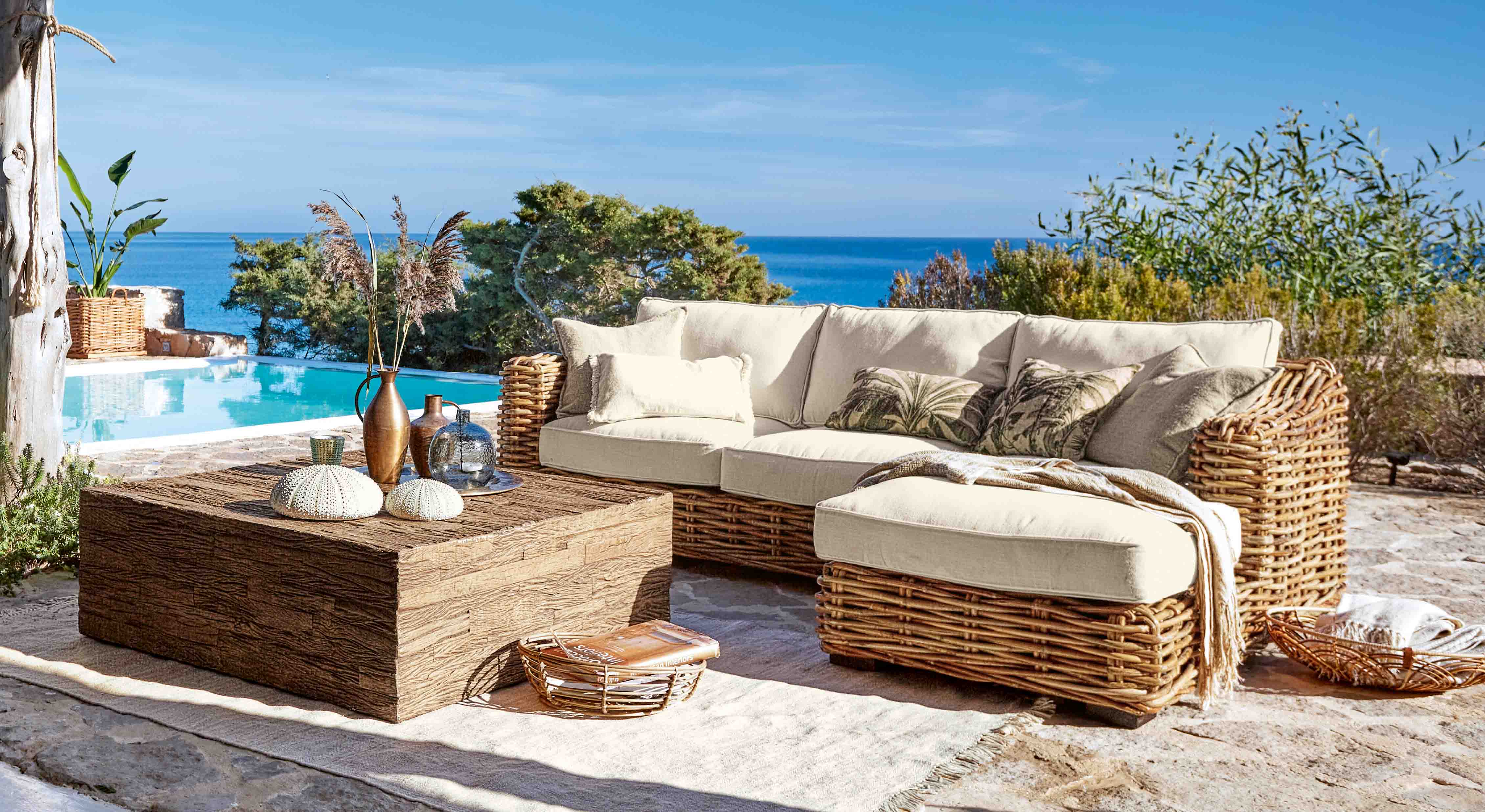 Rattan-Gartenmöbel-Set mit cremefarbenen Polstern am Pool mit Meerblick