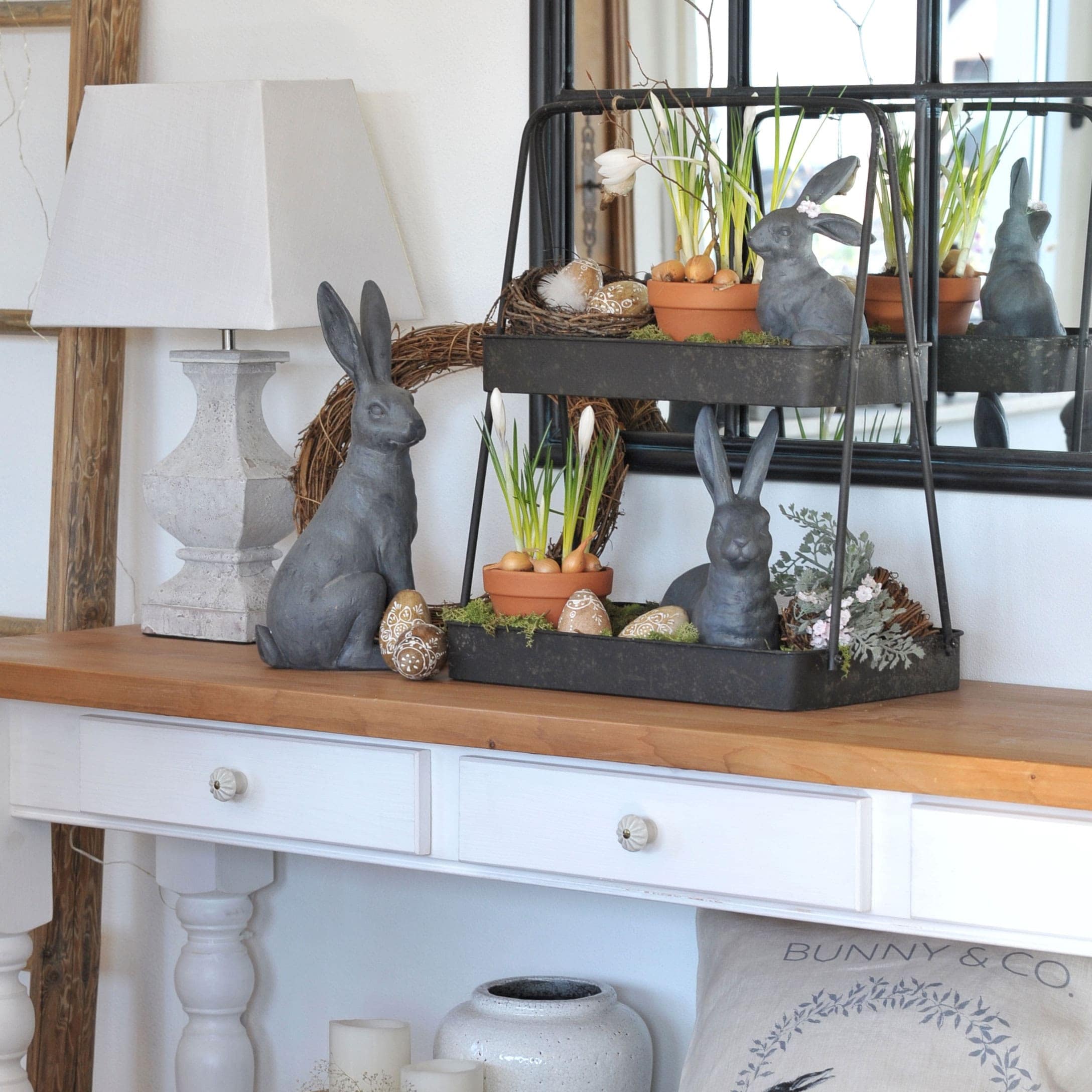 Osterdekoration mit grauen Hasen, Blumentöpfen und verzierten Eiern auf Holztisch