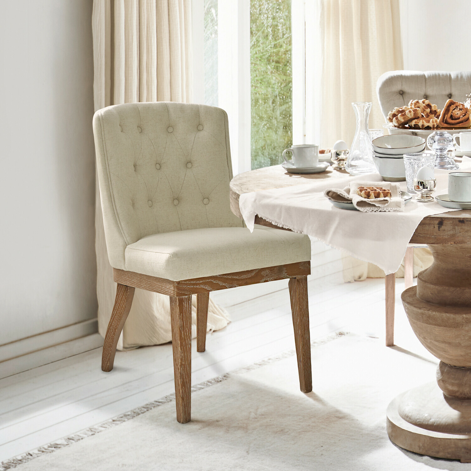 Beiger Polsterstuhl mit Holzbeinen neben einem gedeckten Esstisch mit Geschirr und Gebäck