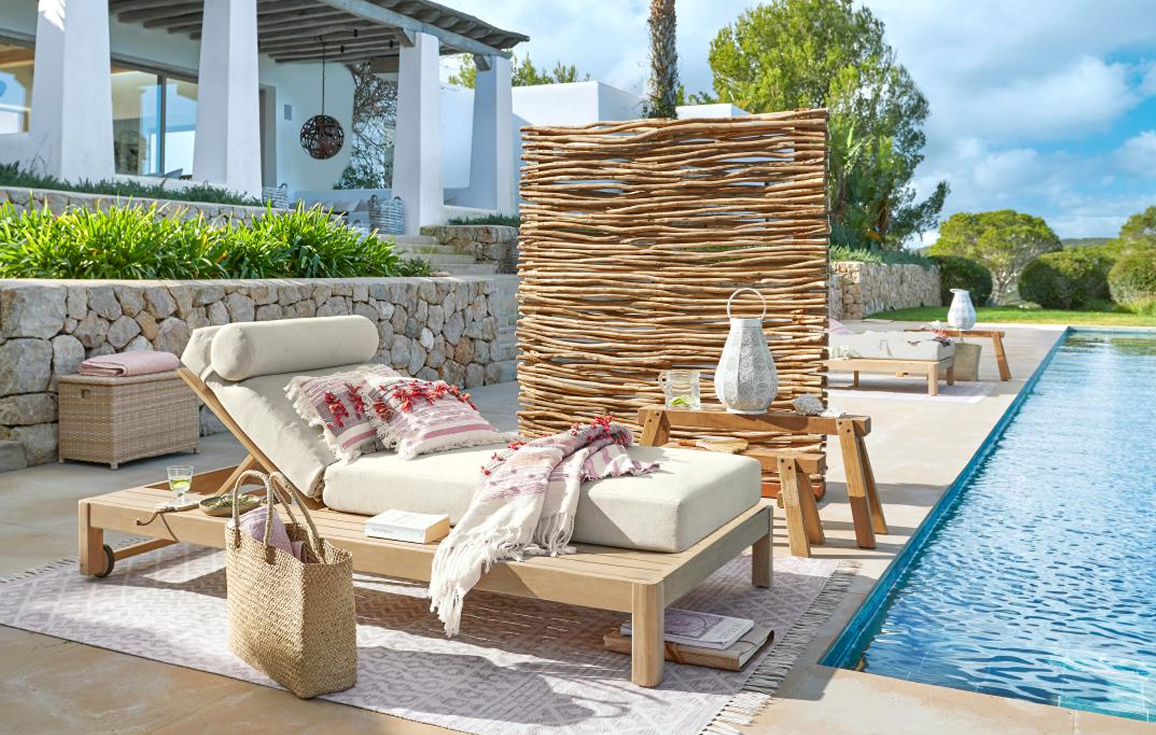 Liege aus hellem Holz mit cremefarbenem Polster und dekorativem Flechtparavent am Pool im maritimen Stil