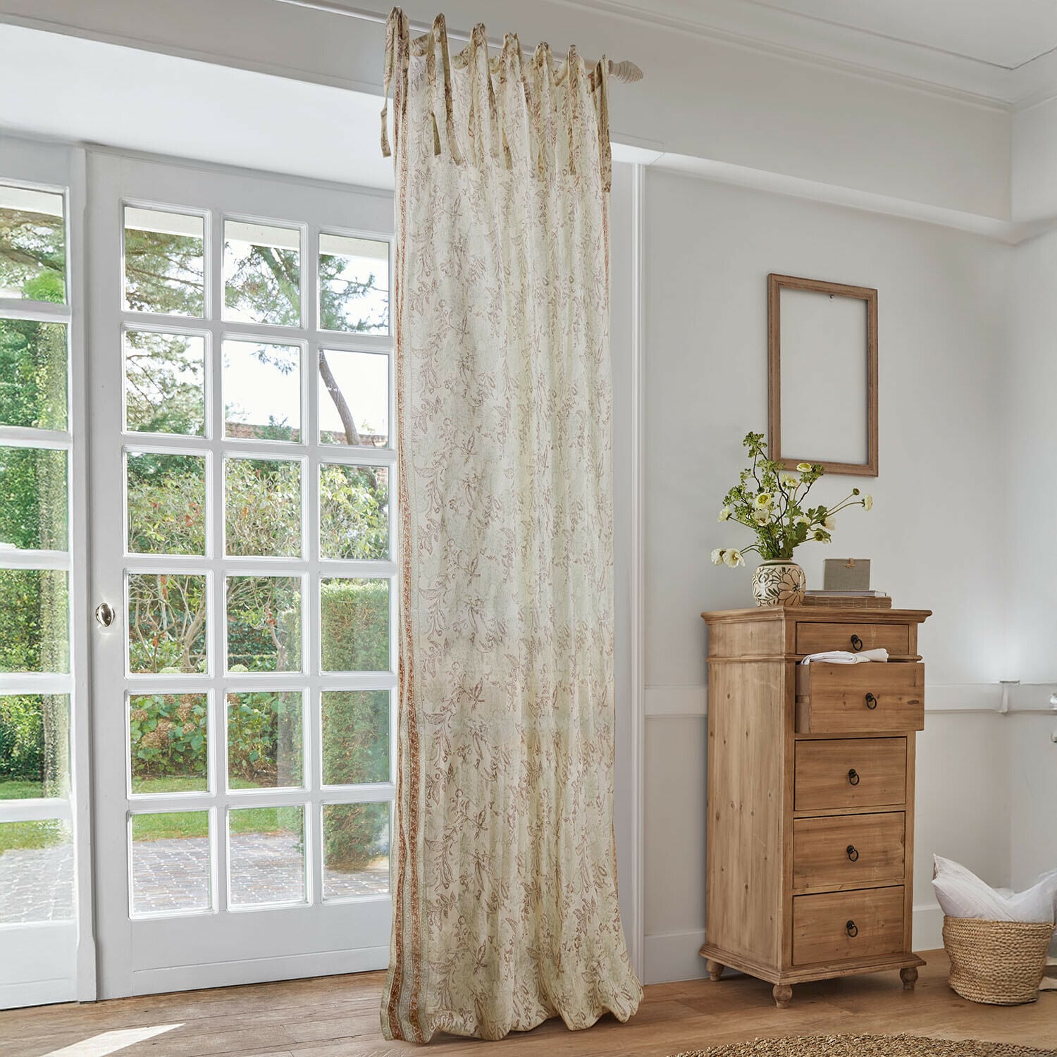 Gardine Floréane Beiger Vorhang mit zartem Blumenmuster in hellem Wohnzimmer mit Holzkommode und großem Fenster