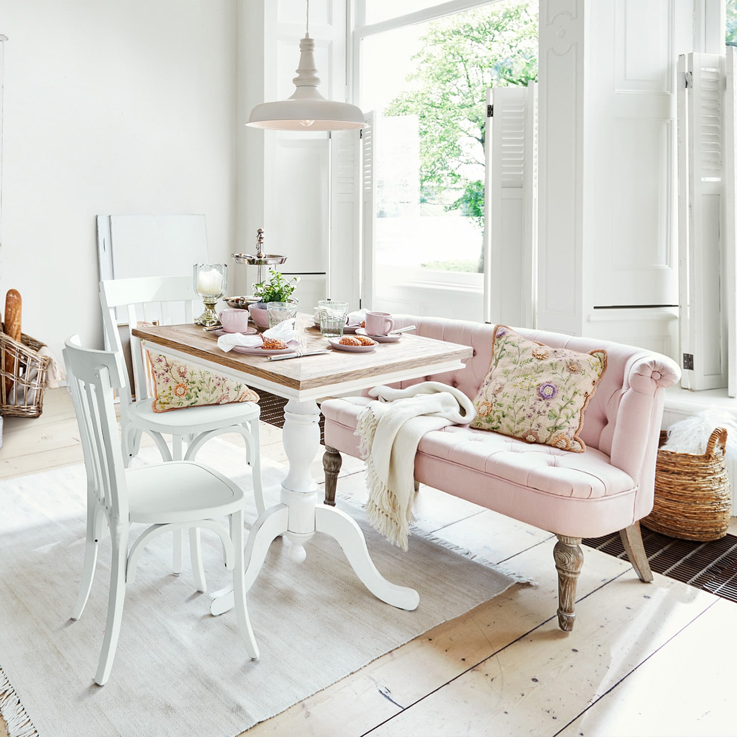 Helles Zimmer mit weißem Holztisch und rosa gepolsterter Bank mit floralem Kissen