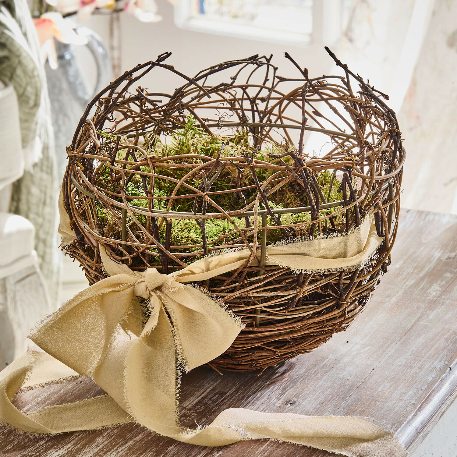 Dekorativer Korb aus Zweigen mit grünem Moos und beigem Band auf Holztisch für Wohnraumgestaltung
