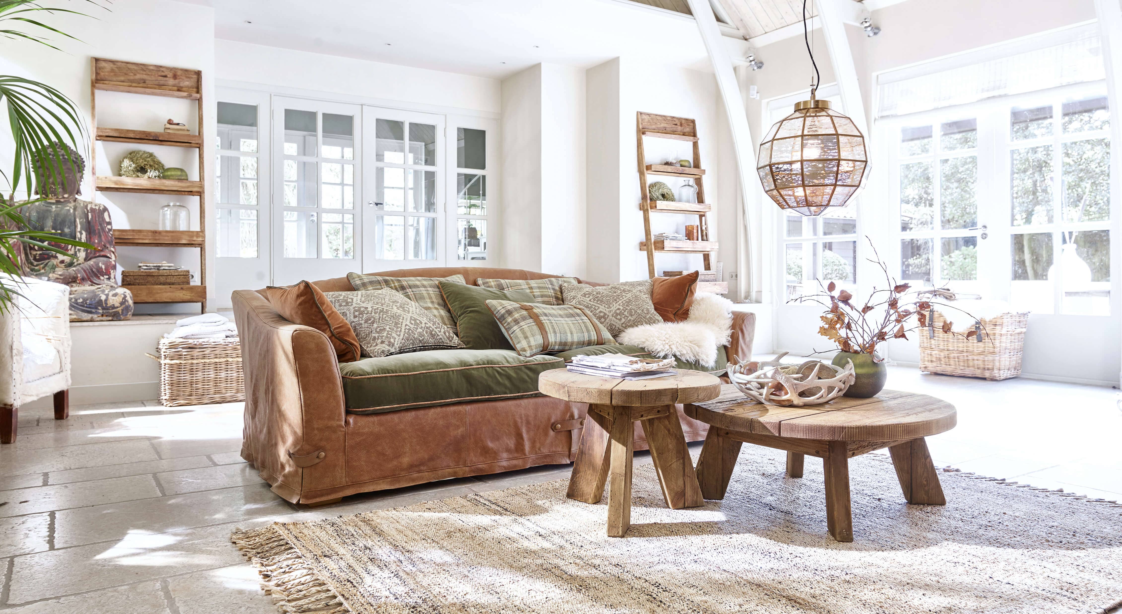 Gemütliches Wohnzimmer mit braunem Ledersofa, grünen Kissen und rustikalen Holztischen