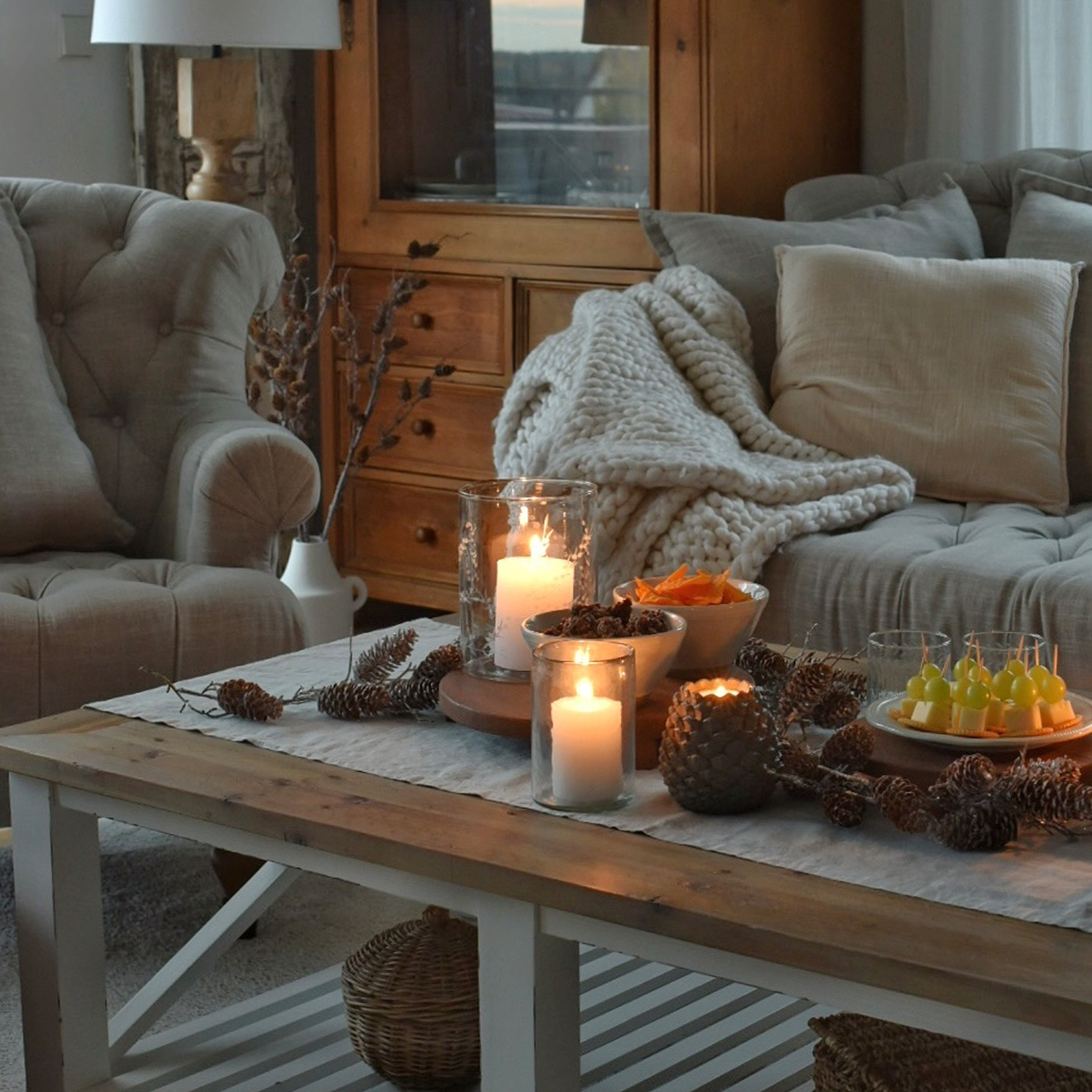 Gemütliches Wohnzimmer mit Holztisch, brennenden Kerzen und grauer Kuscheldecke auf Sofa