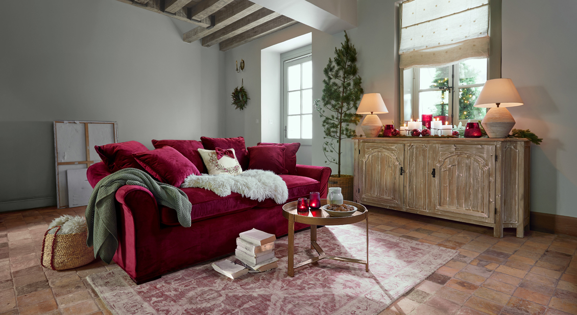 Rotes Samtsofa mit Kissen und Weihnachtsdekoration in gemütlichem Wohnzimmer mit Holztisch