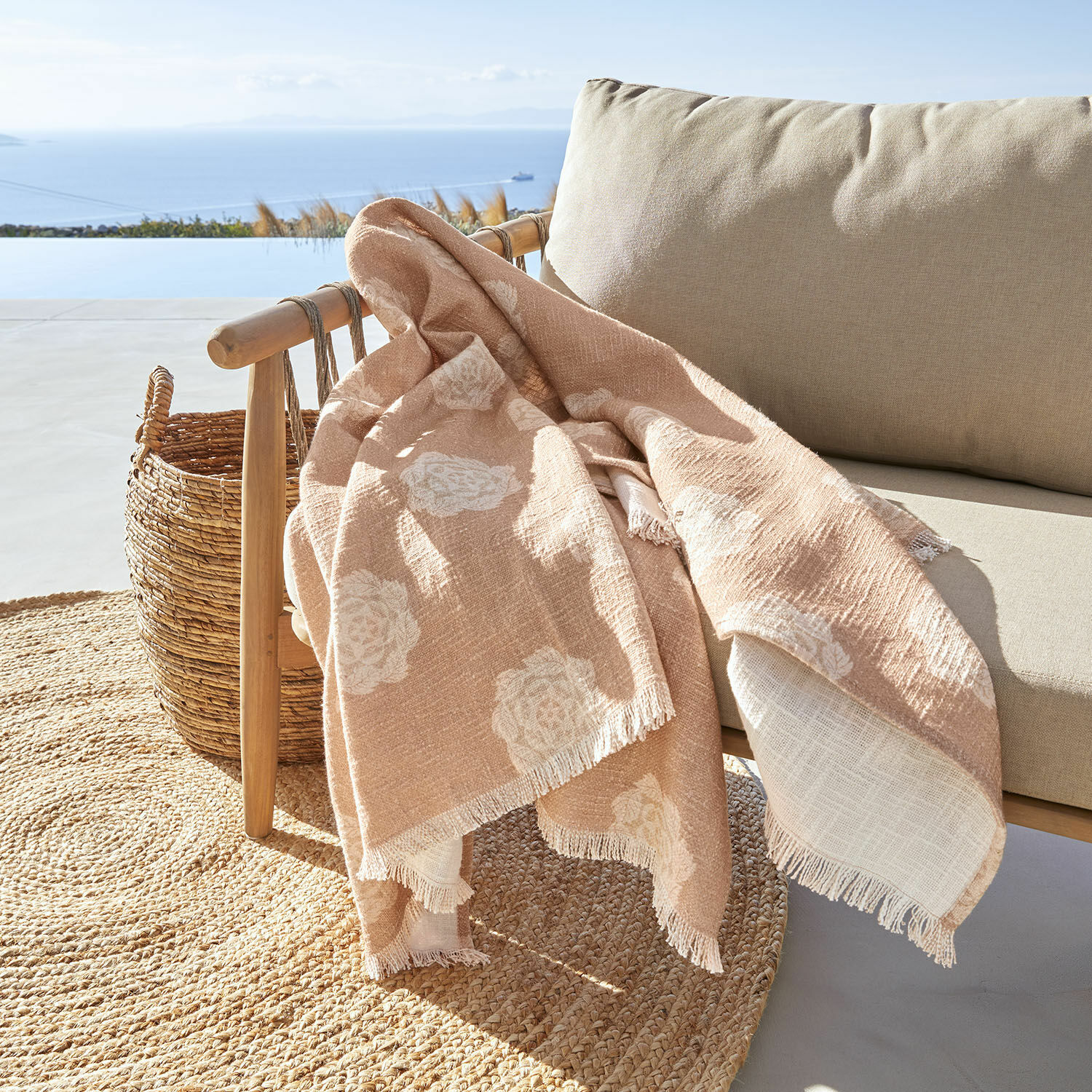 Plaid Belvienne Beige Decke mit weißem Blumenmuster aus weichem Stoff auf Holzstuhl auf Terrasse mit Meerblick
