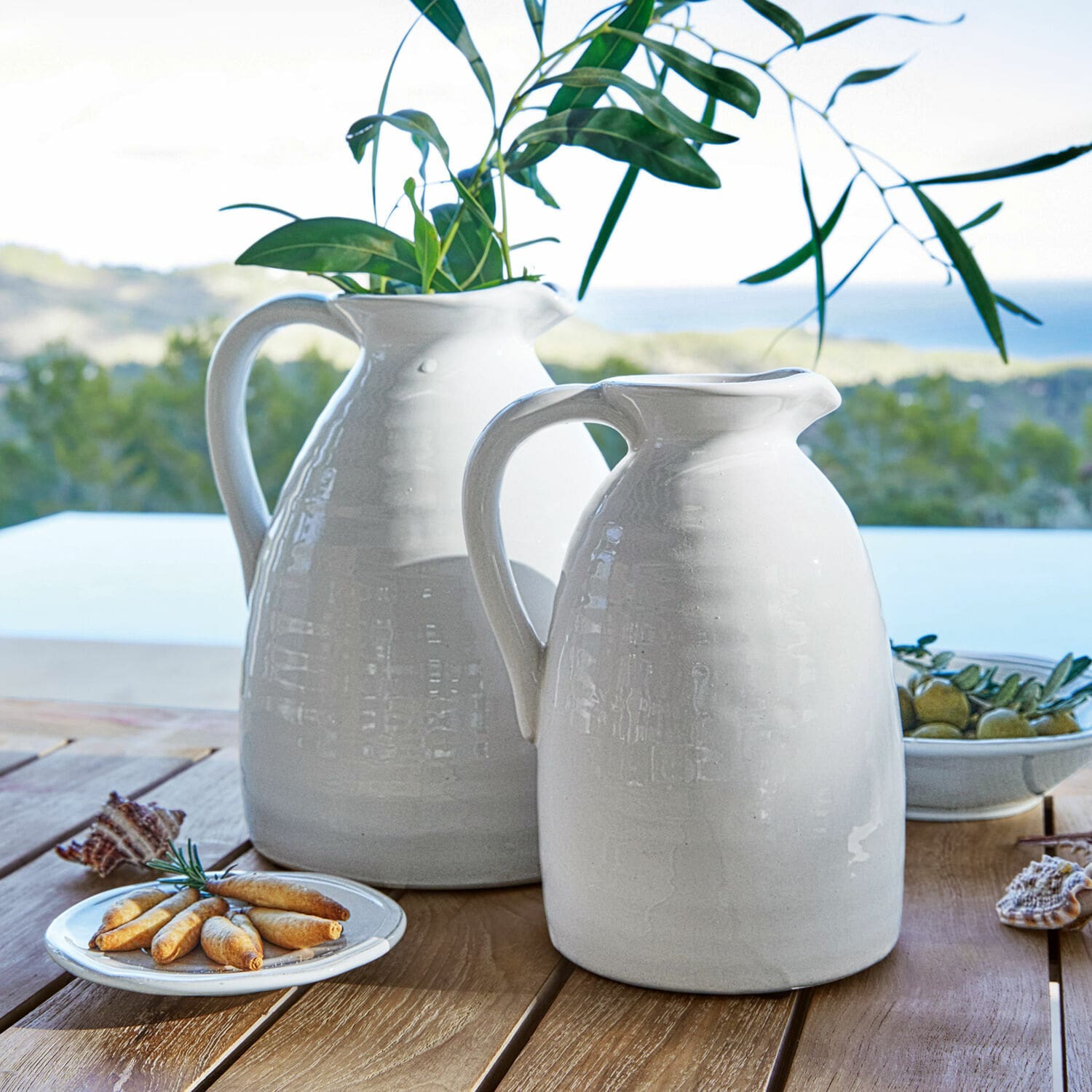 Vase 2er Set Yarick Weiße Keramik-Krüge auf Holztisch mit grünen Blättern und Snacks, Tischdekoration