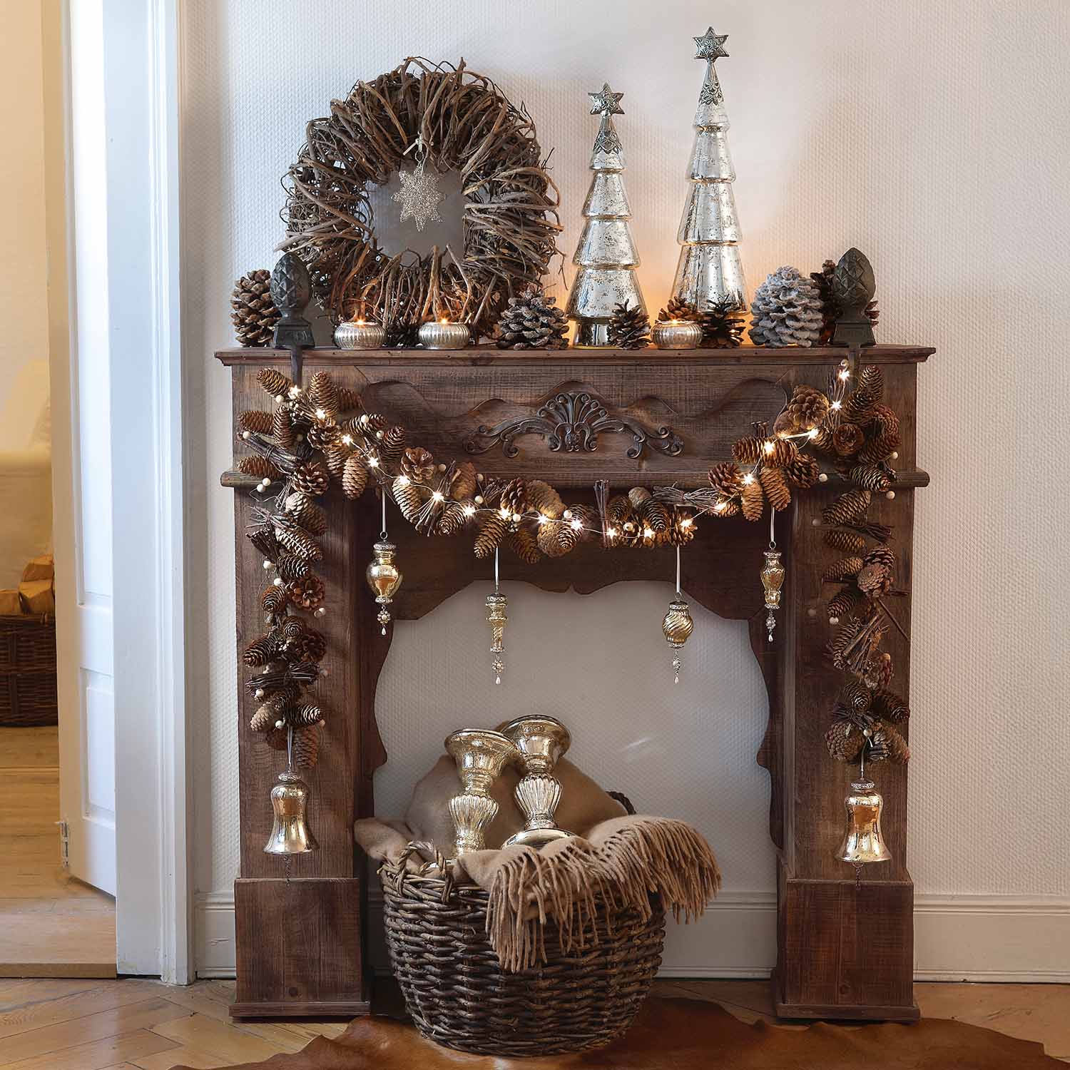 Rustikaler Holz-Kamin mit Tannenzapfen, Lichterkette und silbernen Weihnachtsdekorationen geschmückt
