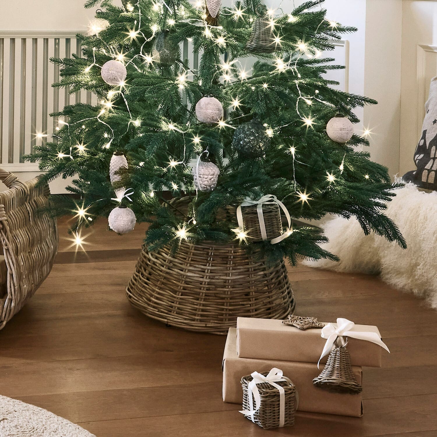 Weihnachtsbaum-Umrandung Kiente Weihnachtsbaum im Korb aus Rattan mit natürlichen Dekorationen und braun verpackten Geschenken auf Holzboden