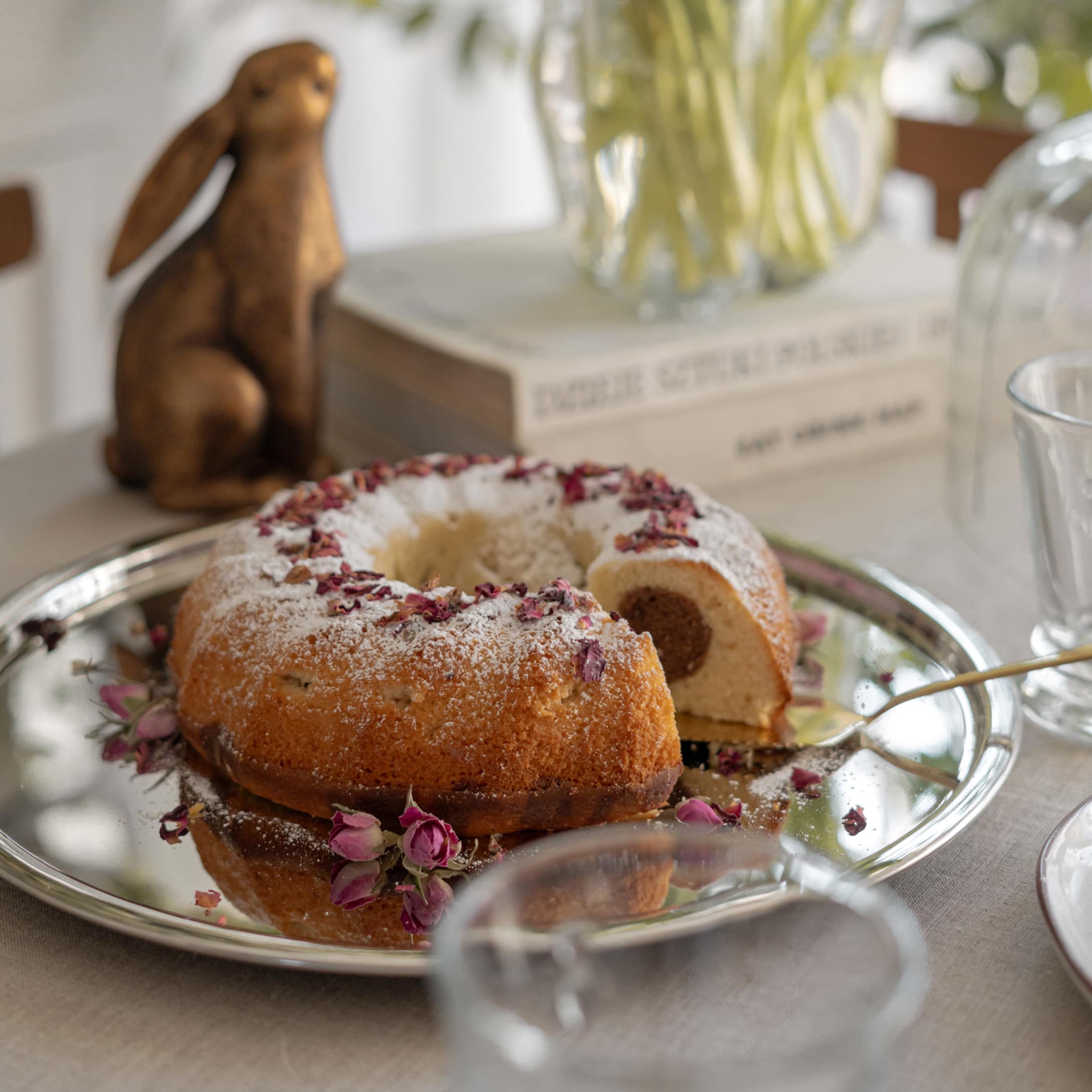 Gugelhupf mit Puderzucker und getrockneten Rosenblättern auf silbernem Tablett auf dem Tisch