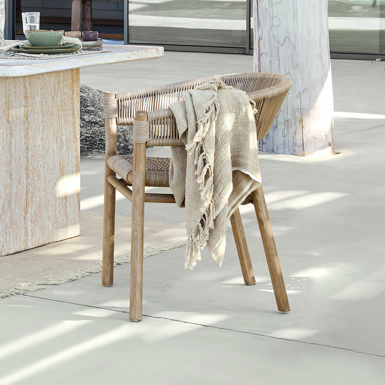 Stuhl FSC®-100% Garmontique Stuhl aus Holz und Naturseil in hellem Farbton mit beigem Plaid vor hellem Boden und Tisch