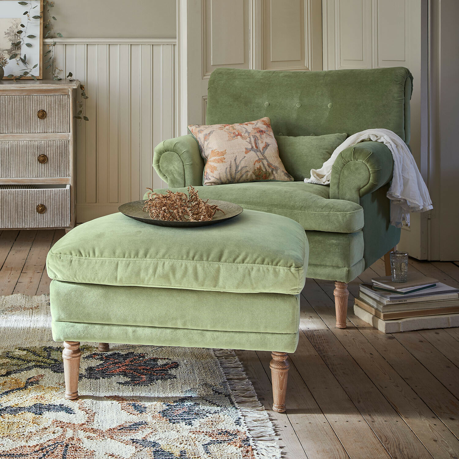 Grüner Samtfotel mit Hocker auf Holzbeinen in gemütlichem Wohnzimmer mit Teppich