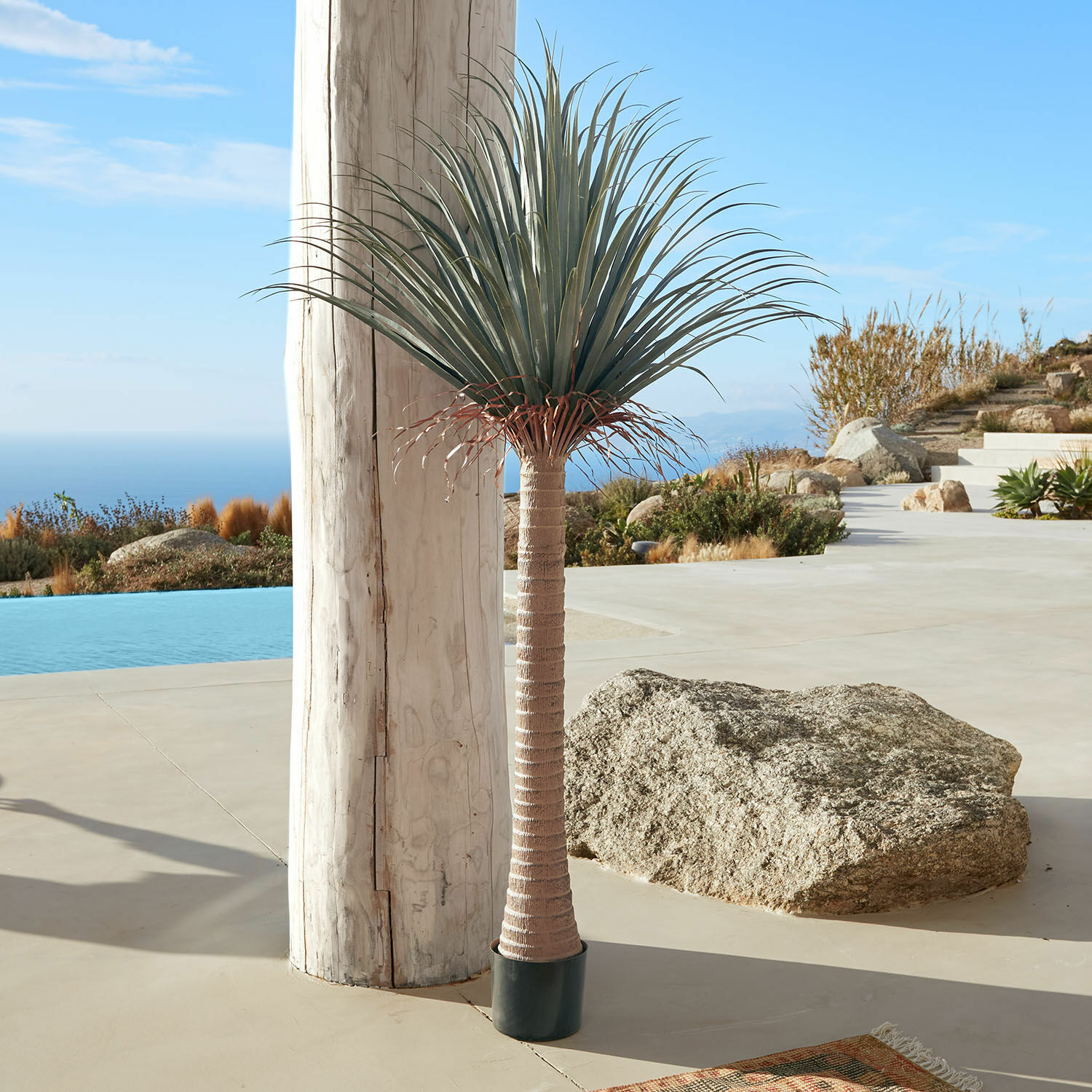 Deko-Palme Remivon Künstliche Palme im Topf mit braunem Stamm und grünen Blättern auf Terrasse mit Meerblick