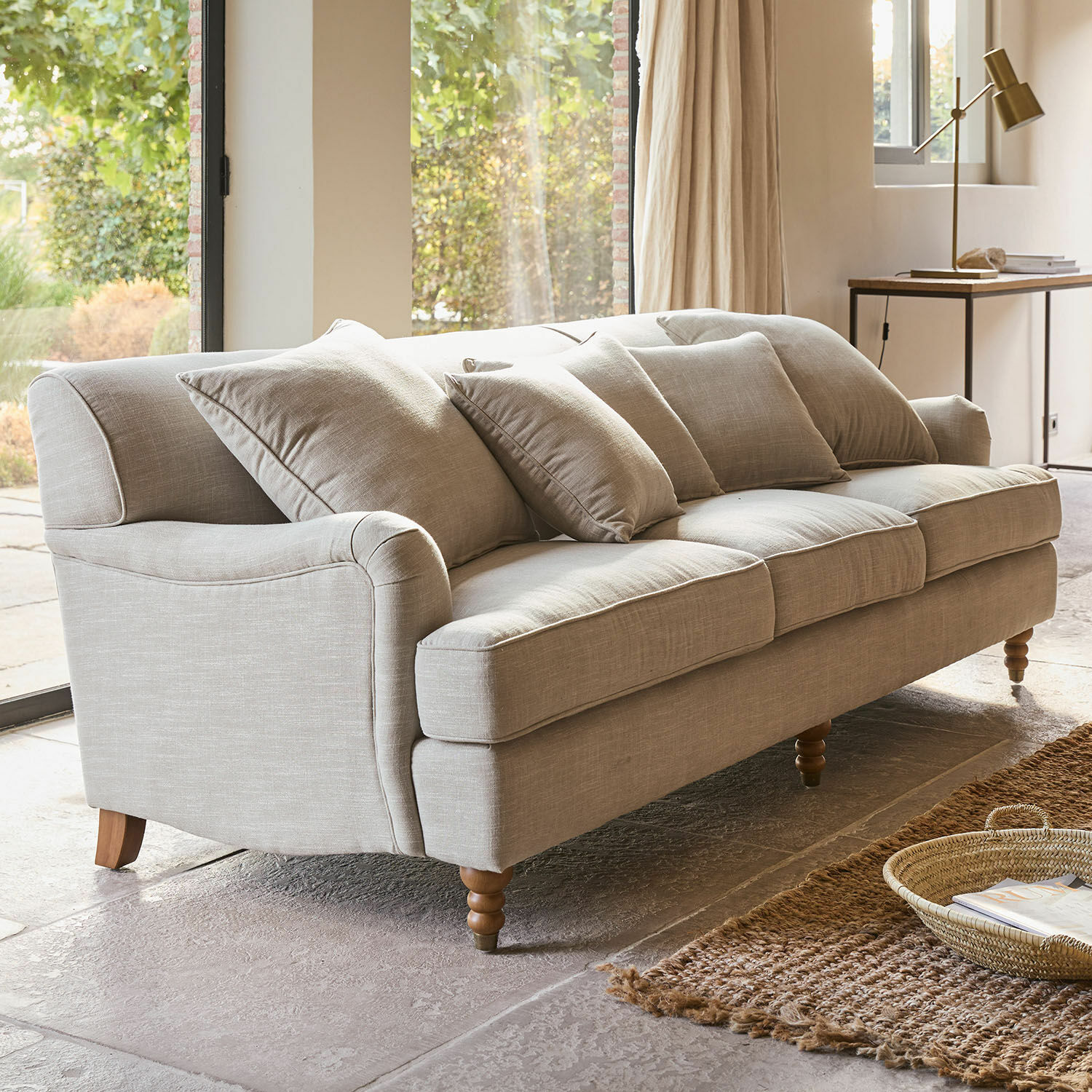 Sofa Isa Beige bezogener Sofa mit Kissen und Holzbeinen in hellem Wohnzimmer mit Teppich