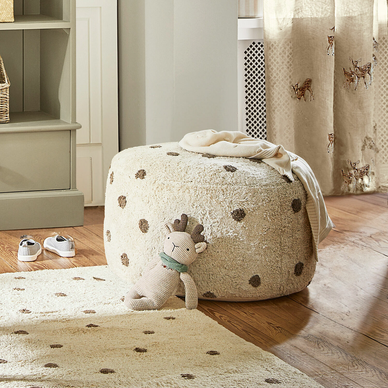 Pouf Thivalie Beiger, weicher Polsterhocker mit Punkten auf Holzboden, Kuscheltier und Teppich im Raum