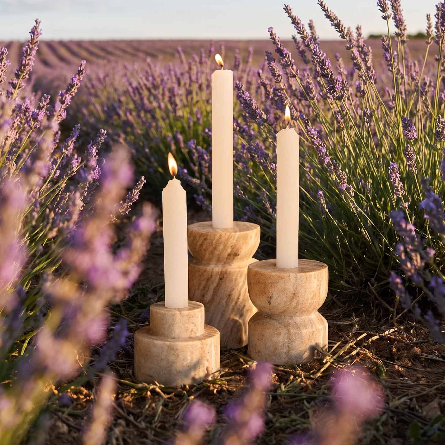 Drei cremefarbene Kerzen in natürlichen Holzkerzenhaltern auf einem Lavendelfeld bei Sonnenuntergang