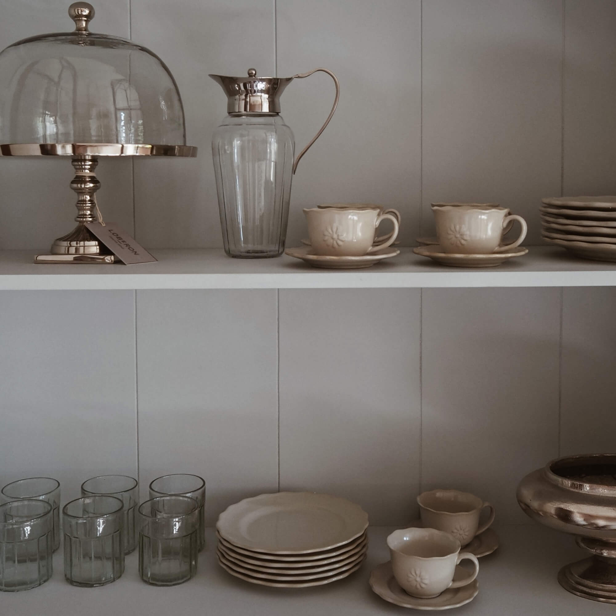 Set aus cremefarbener Keramik mit Tassen und Tellern sowie Glas-Krug mit Metallgriff auf Regal