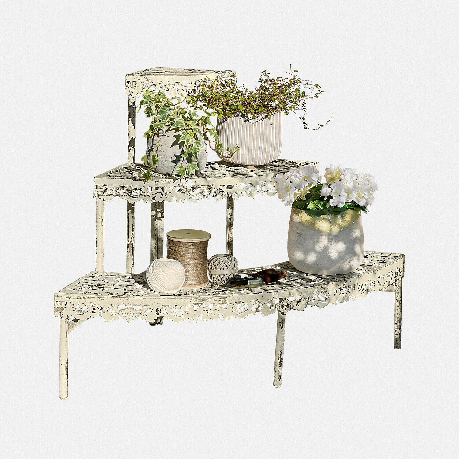 Metallregal in Creme mit filigranem Muster, Pflanzen und Gartengeräten vor weißem Hintergrund