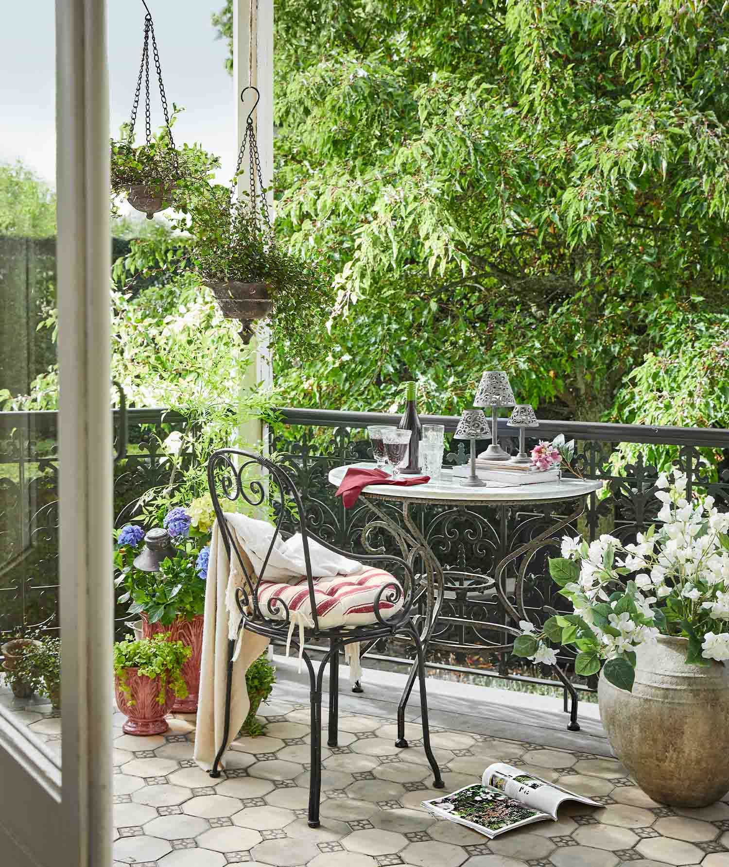 Balkon mit schmiedeeisernem Tisch und Stuhl mit gestreiftem Kissen, umgeben von grünen Pflanzen und Blumentöpfen