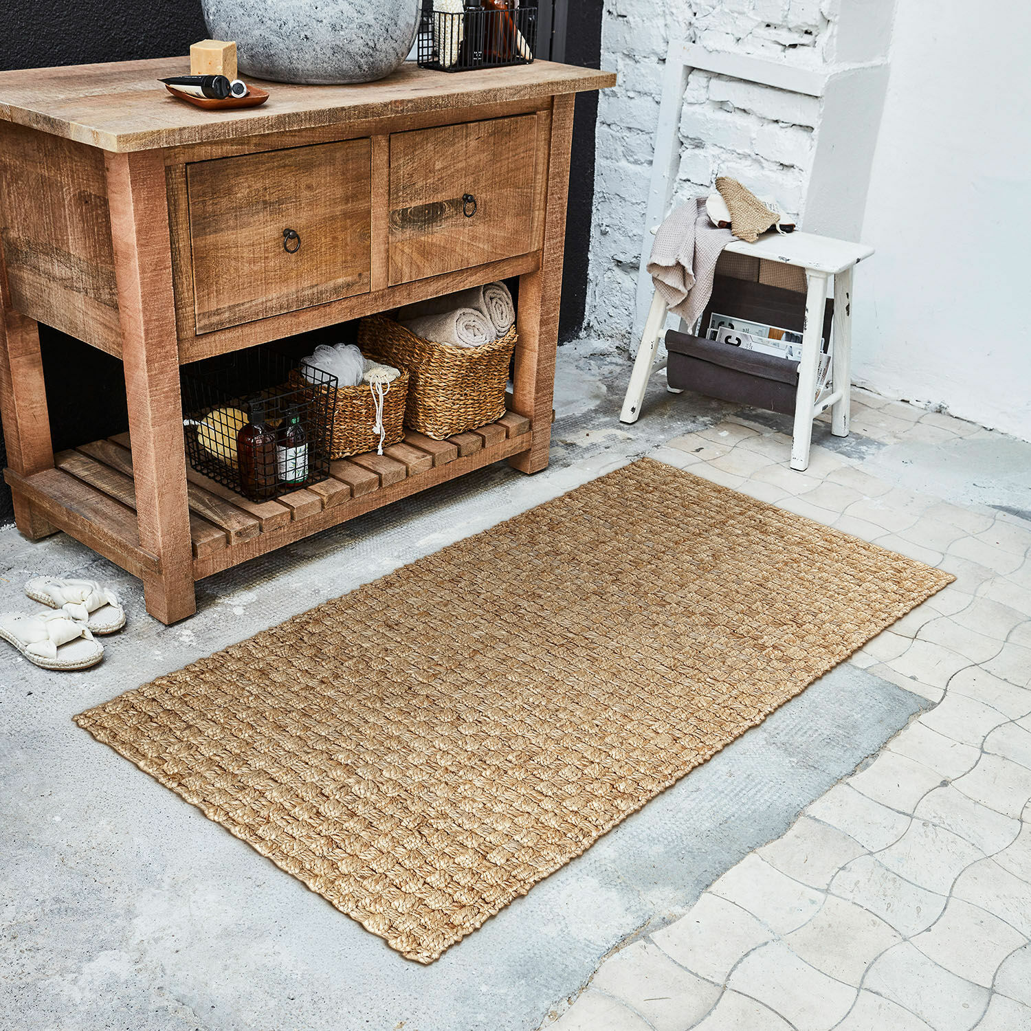 Läufer Daoukro Beiger Teppich aus natürlicher Jute auf Boden neben Holzkommode und weißem Hocker