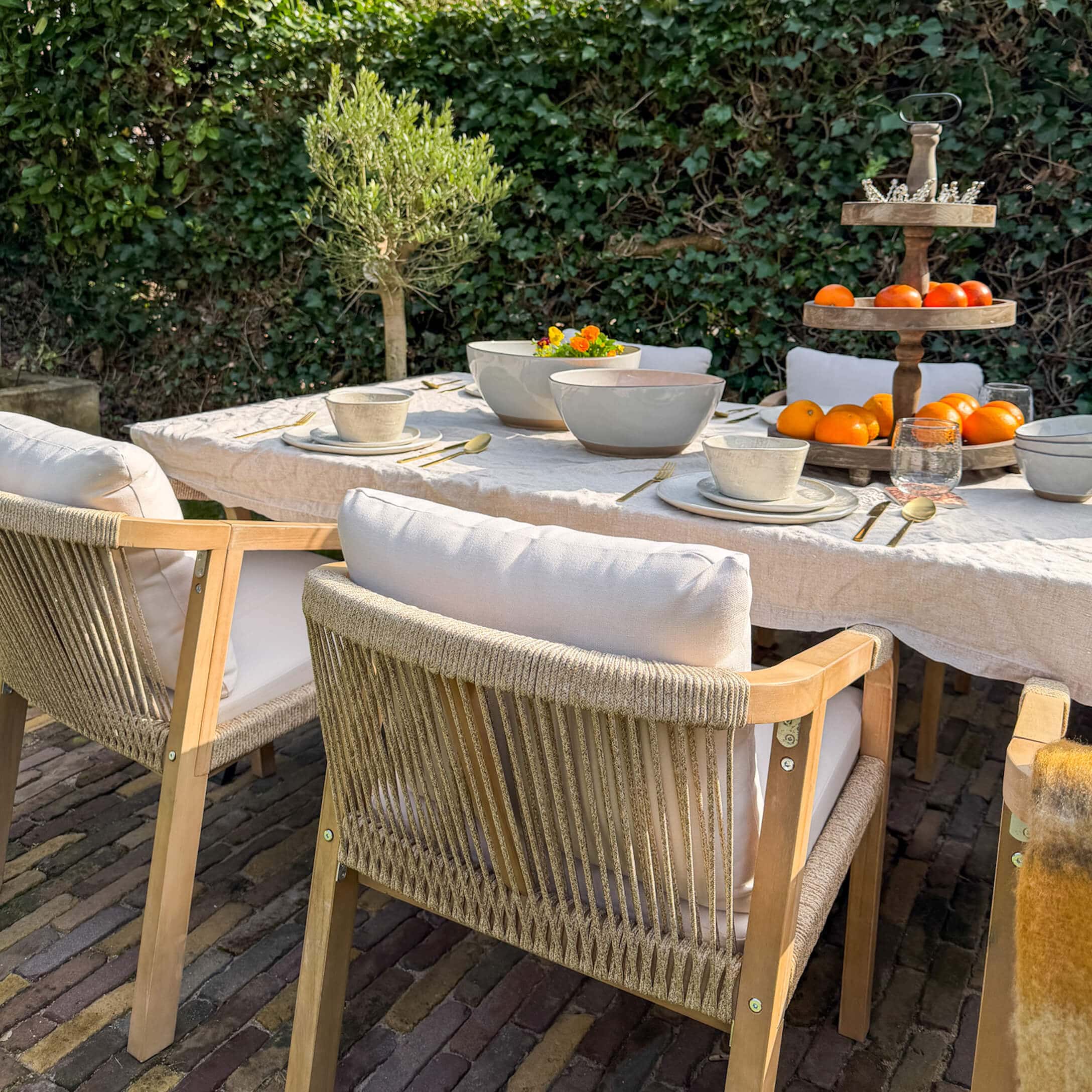 Gartenmöbel-Set mit Holzstühlen und weißen Kissen an gedecktem Tisch mit Geschirr und Obst