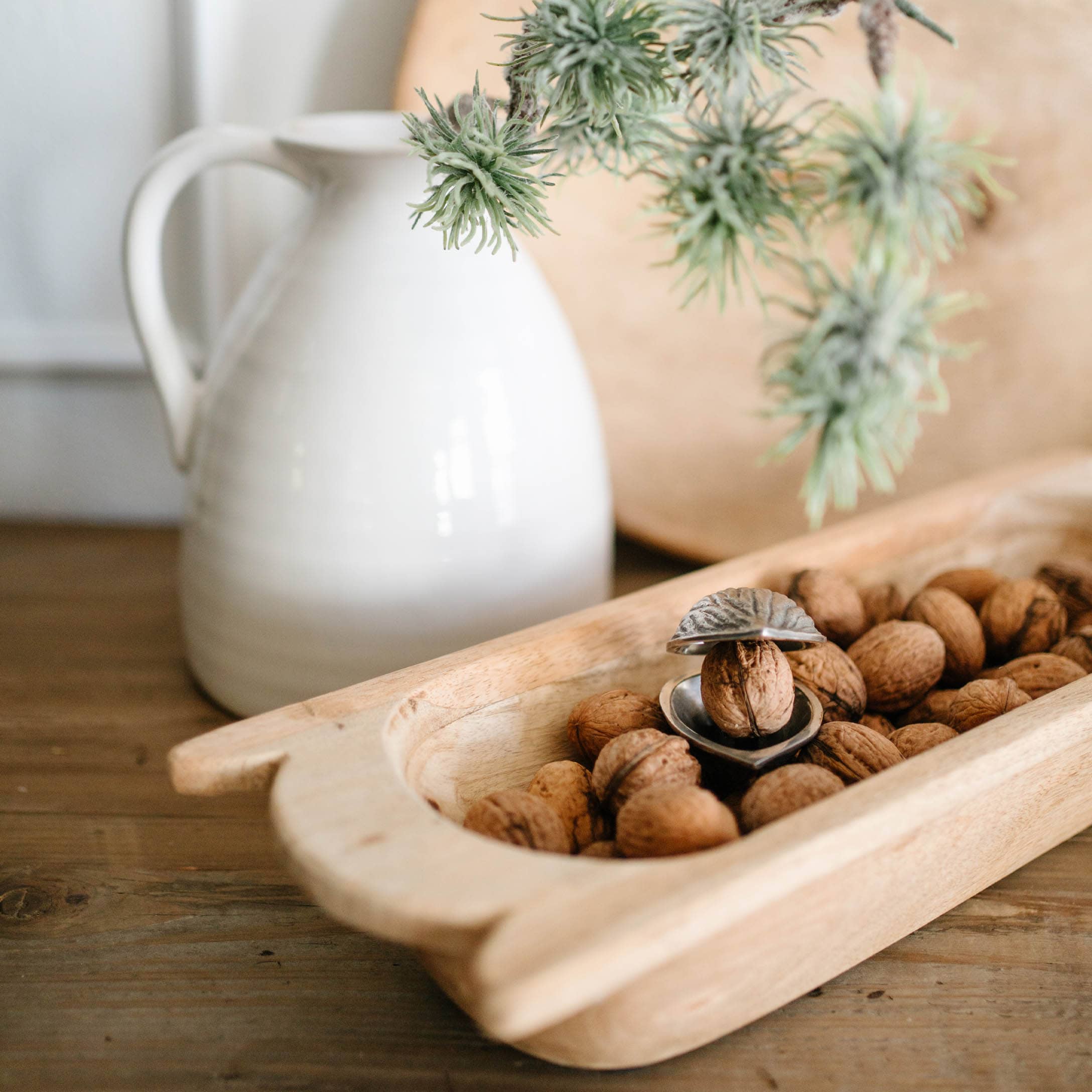 Holztablett mit Walnüssen und Metall-Nussknacker auf Holztisch neben weißem Krug