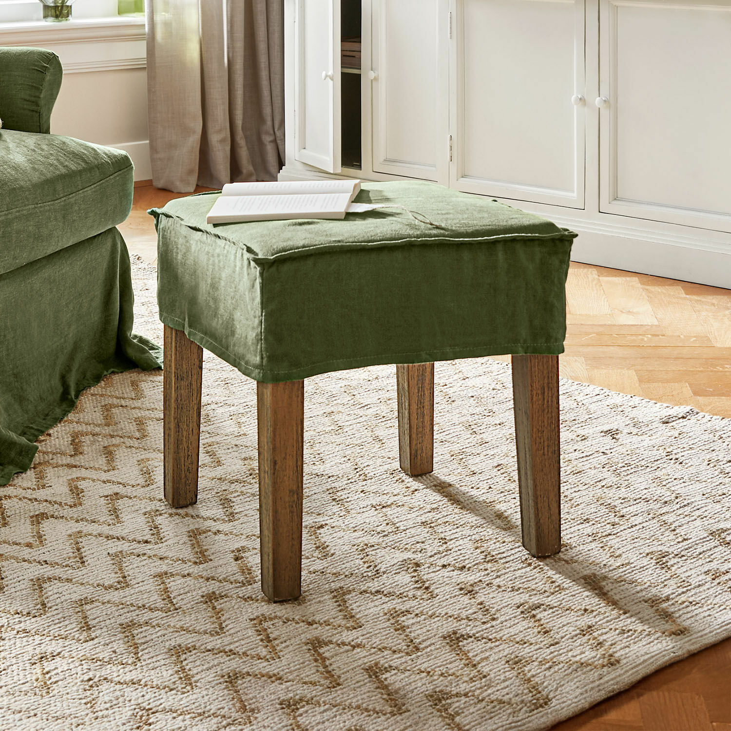Hocker Vionnique Grüner Hocker mit Leinenbezug und Holzbeinen auf hellem Teppich im Wohnzimmer