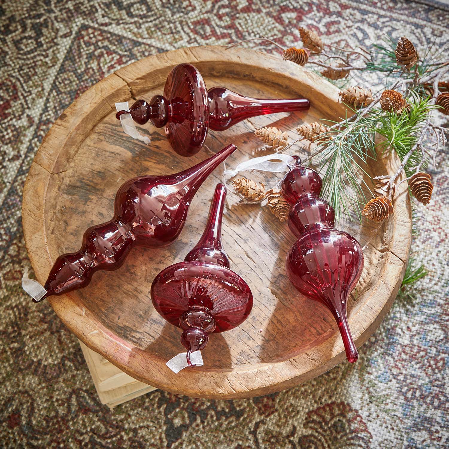 Vier rote Glas-Weihnachtsornamente auf einem Holztablett mit Zweigen und Kiefernzapfen
