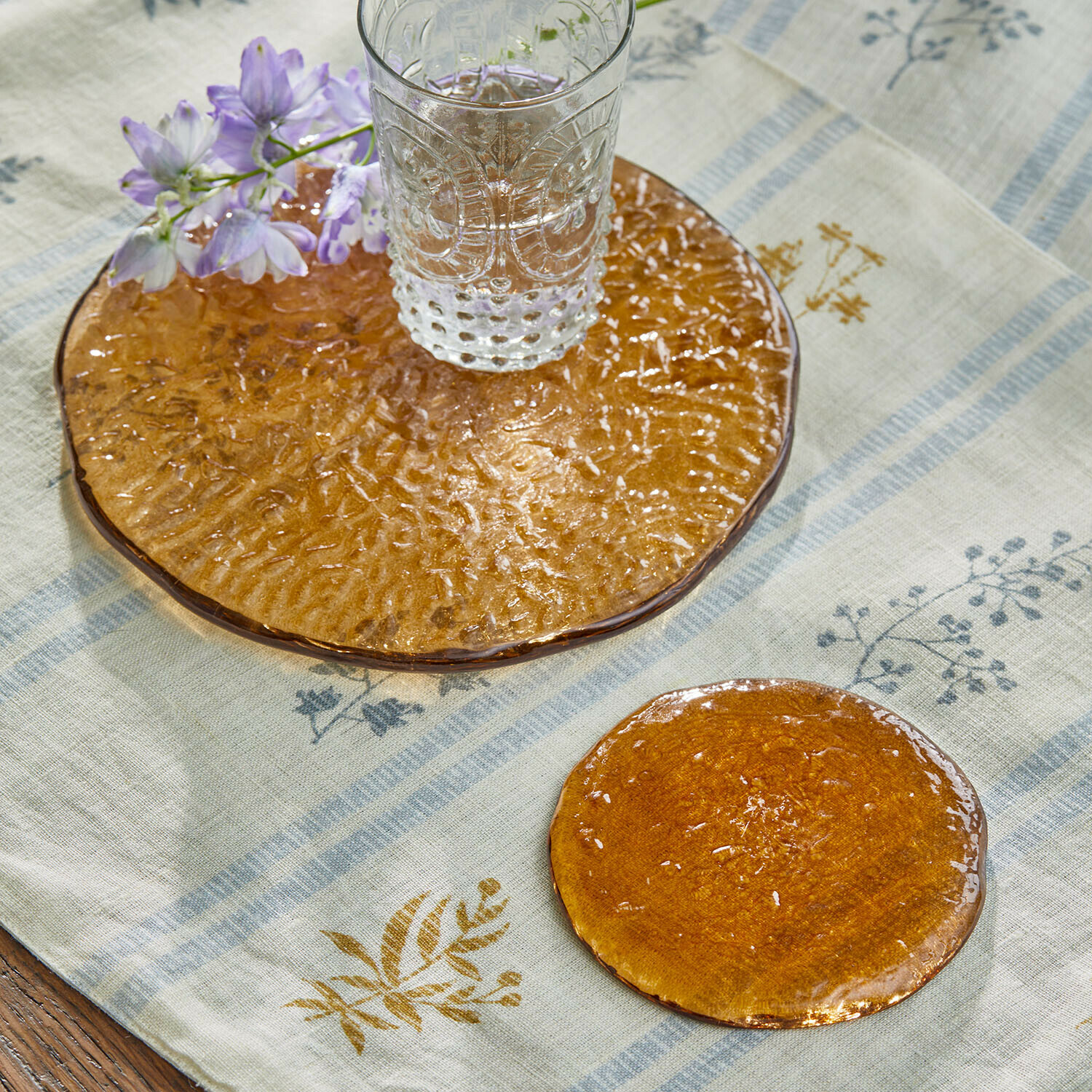 Transparentes Glas auf orangefarbenem Glasuntersetzer mit Blume auf Leinentischdecke
