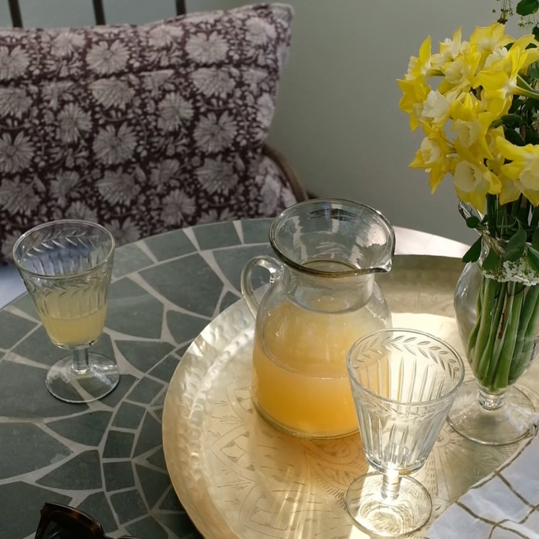 Glaskrug mit gelbem Getränk und zwei Gläser auf Marmor-Tisch mit Blumen in Vase