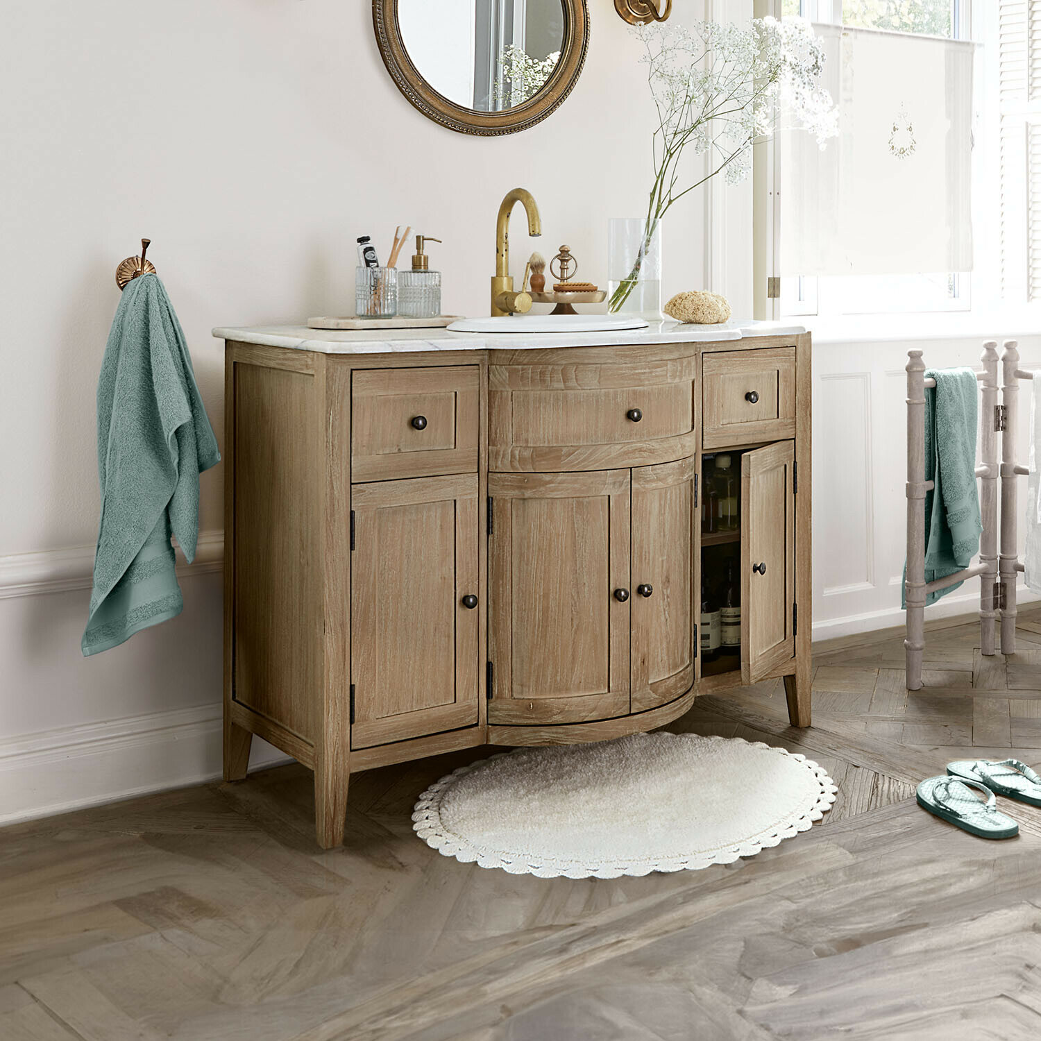 Holz-Badezimmerschrank mit Marmorplatte, goldener Armatur, mintfarbene Handtücher und runder Teppich