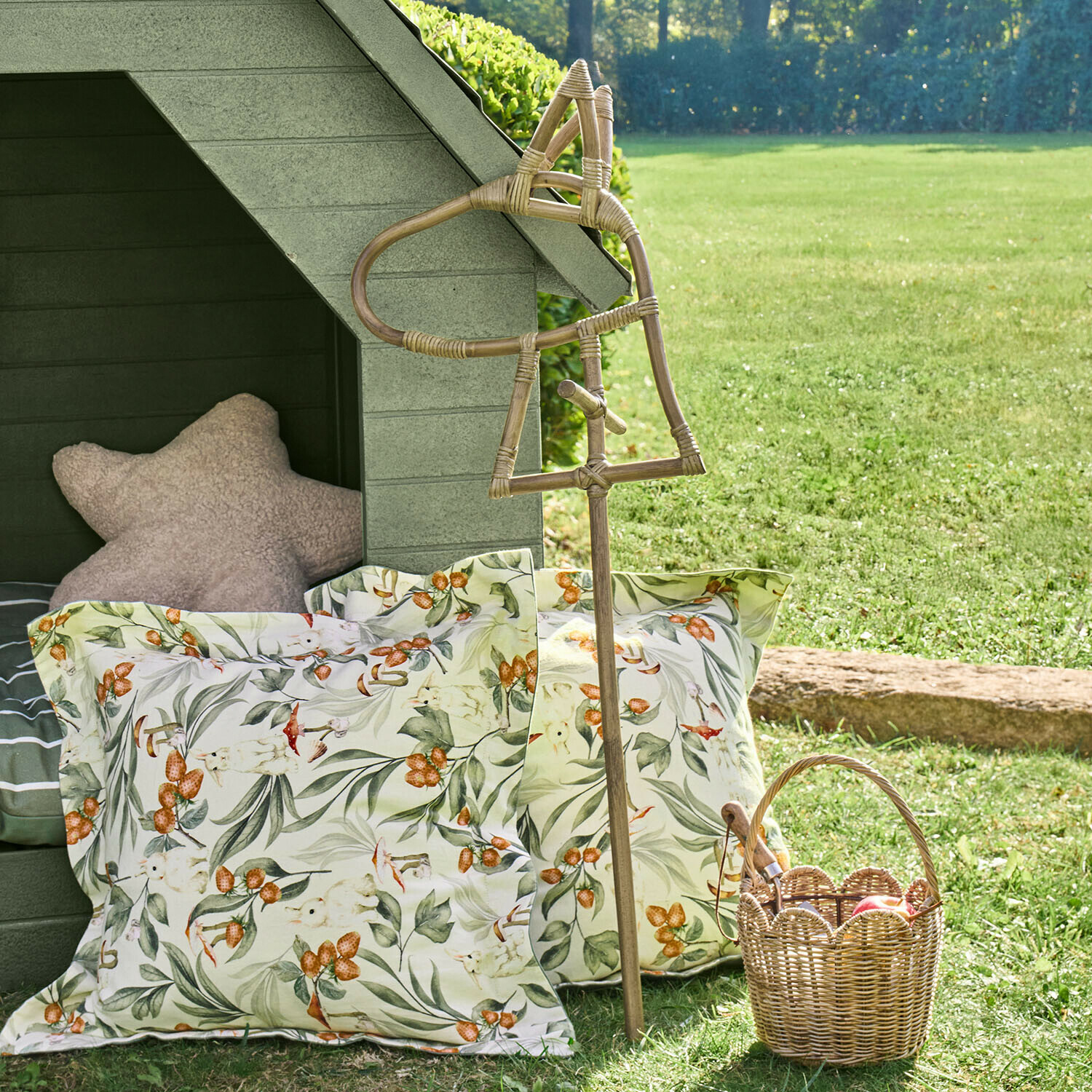 Dekorativer Rattanstab in Pferdeform vor floral gemusterten Kissen und einem Korb aus Weide im Garten