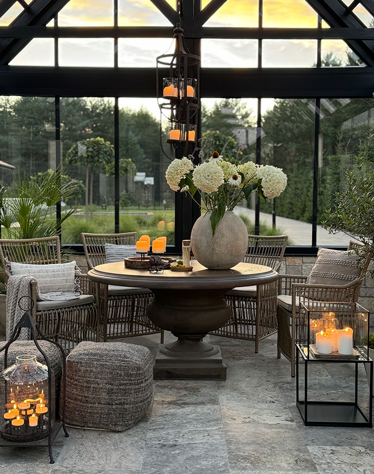 Gemütlicher Wintergarten mit runden Tisch, Rattanstühlen und Kerzenlicht-Dekoration auf Steinboden