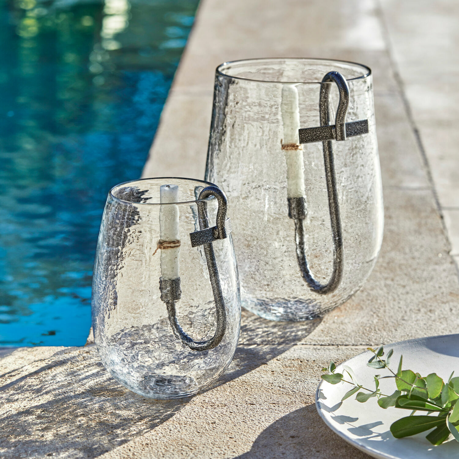 Glaslaternen mit Metallgriff und weißer Kerze am Poolrand, stilvolle Gartendekoration