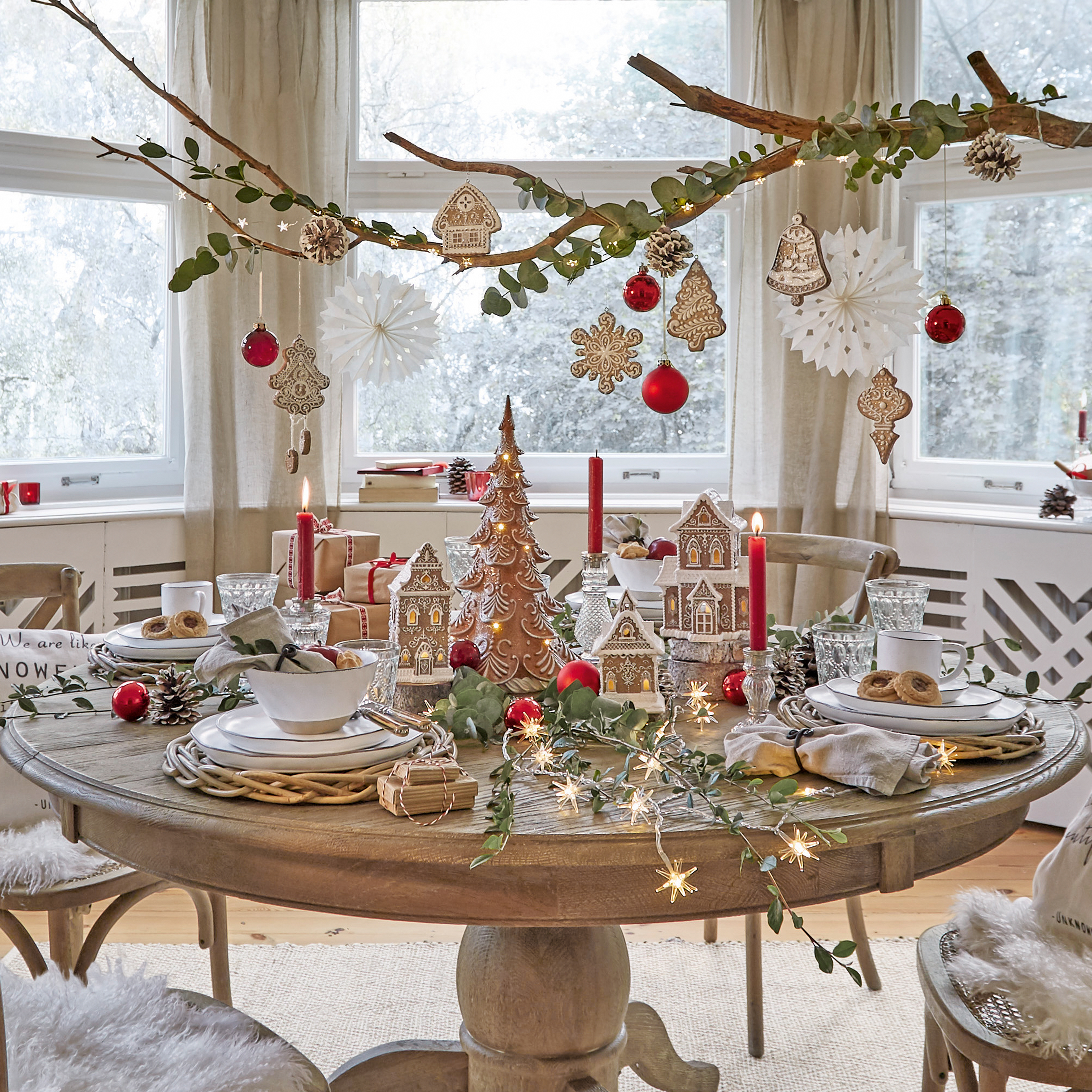 Runder Holztisch mit Weihnachtsdeko aus Lebkuchenhäusern, roten Kugeln und brennenden Kerzen