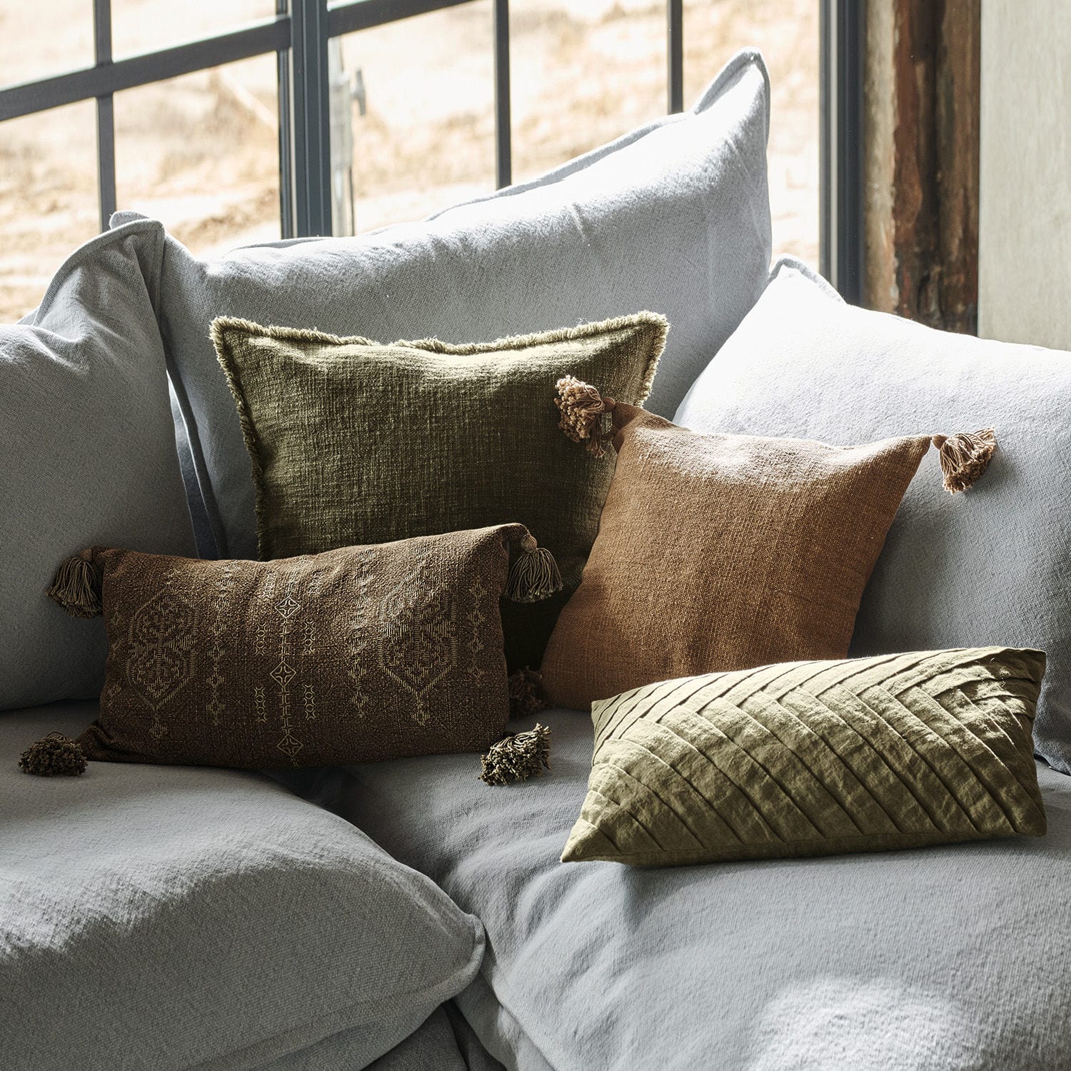 Kissenhülle 4er Set Donagh Dekorative Kissen aus Stoff in Braun- und Grüntönen auf grauem Sofa arrangiert