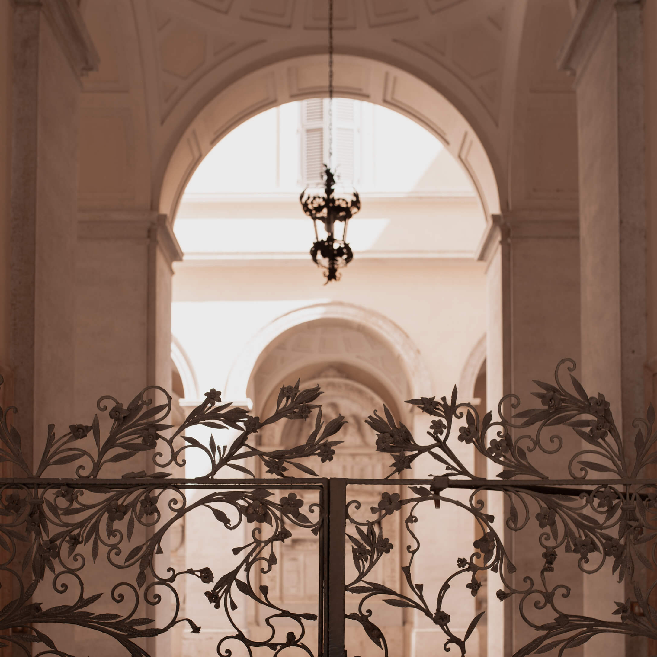 Verzierte schmiedeeiserne Tor mit floralem Muster vor hellem Bogen und hängender Lampe