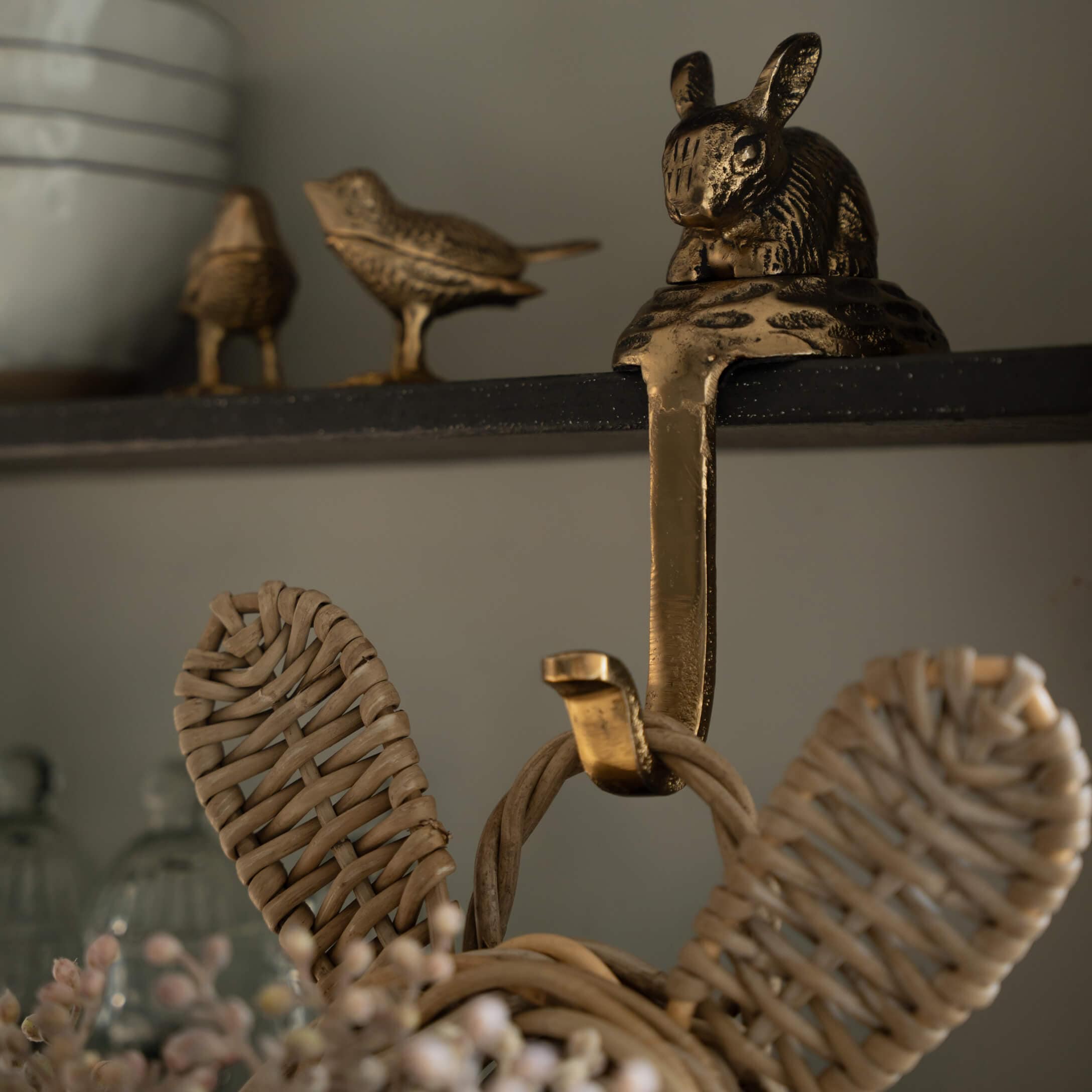 Goldfarbener Messinghaken mit Hasen- und Vogelmotiv an schwarzem Regal für Wohnraum