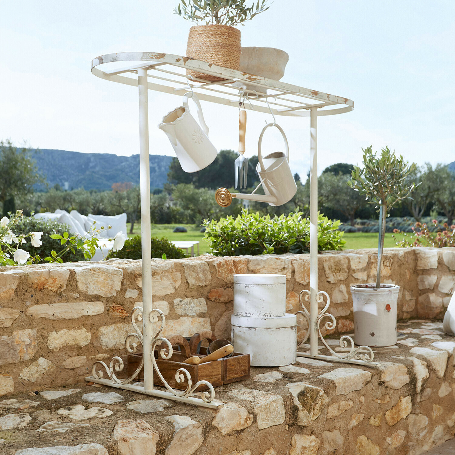Pflanztisch-Gestell Mairoux Weiße Metall-Gartenablage mit hängenden Accessoires und Blumentopf auf Steinmauer im Garten