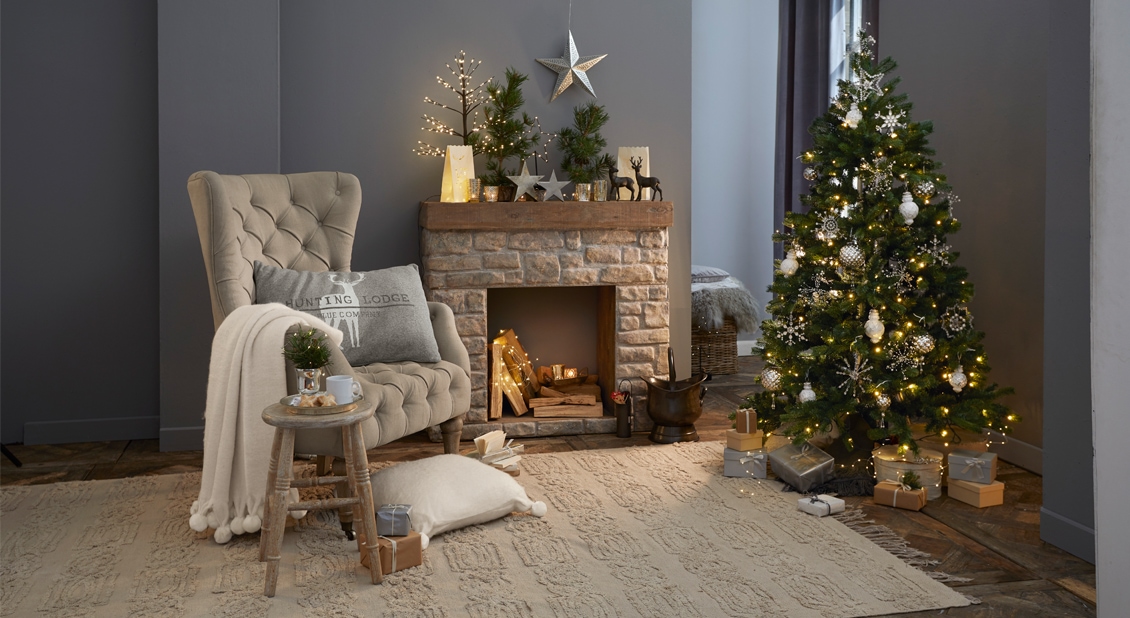 Gemütliches Wohnzimmer mit beigem Sessel, Steinkamin und festlich geschmücktem Weihnachtsbaum