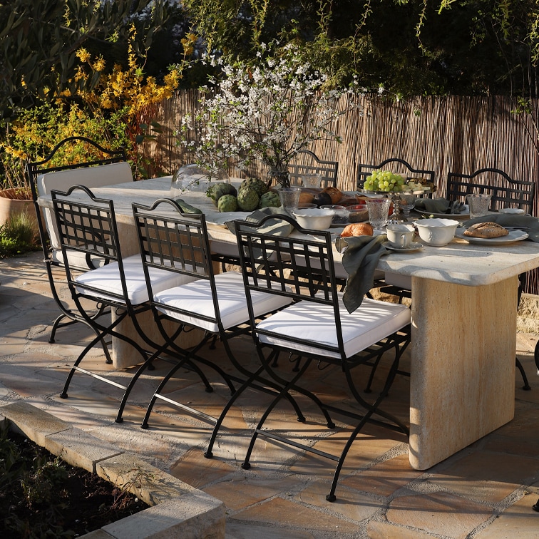 Gartentisch aus Stein mit schwarzen Metallstühlen und weißen Sitzkissen, gedeckt für Mahlzeit im Freien
