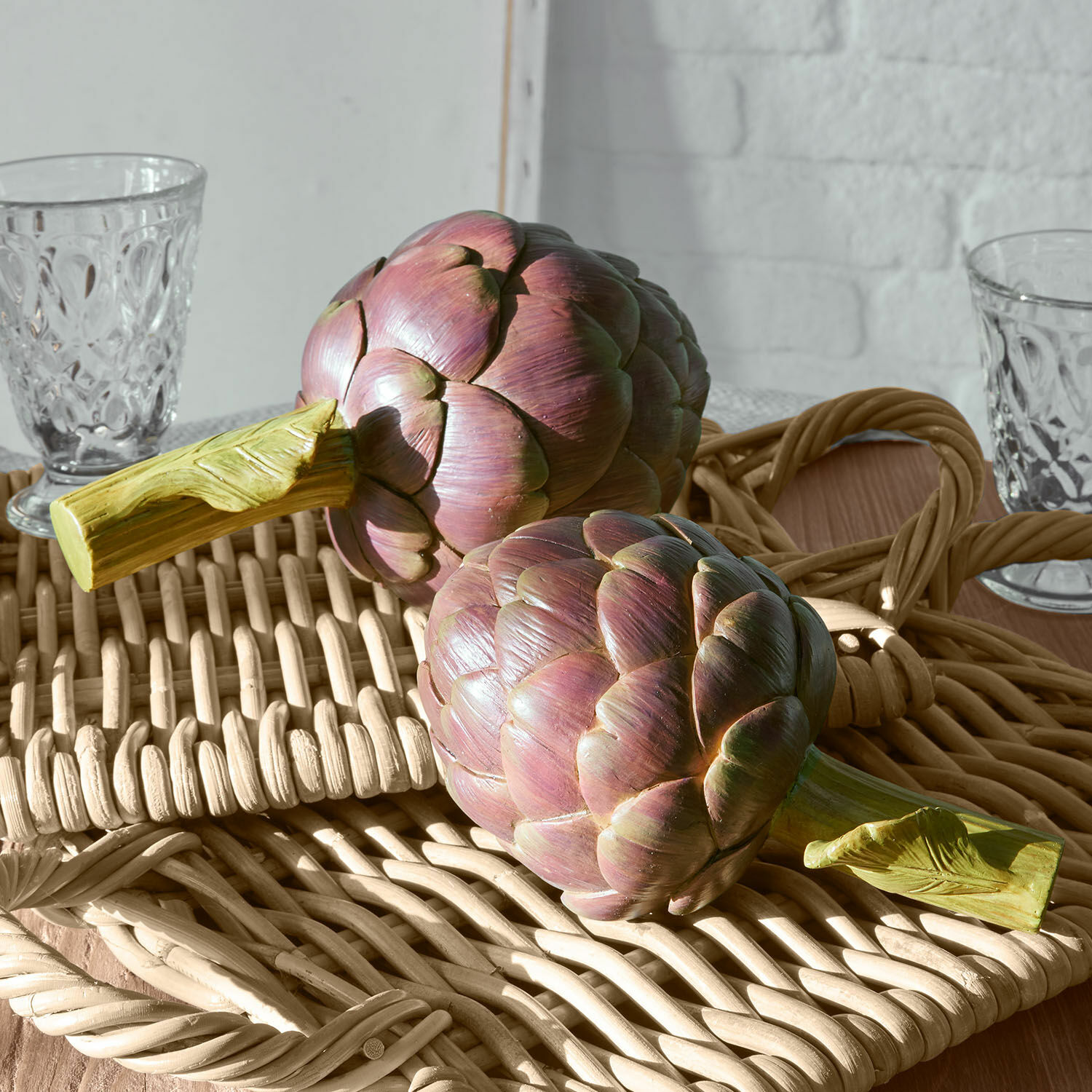 Dekorative Artischocken aus Kunststoff in Violett-Grün auf einem geflochtenen Tablett als Wohnaccessoire