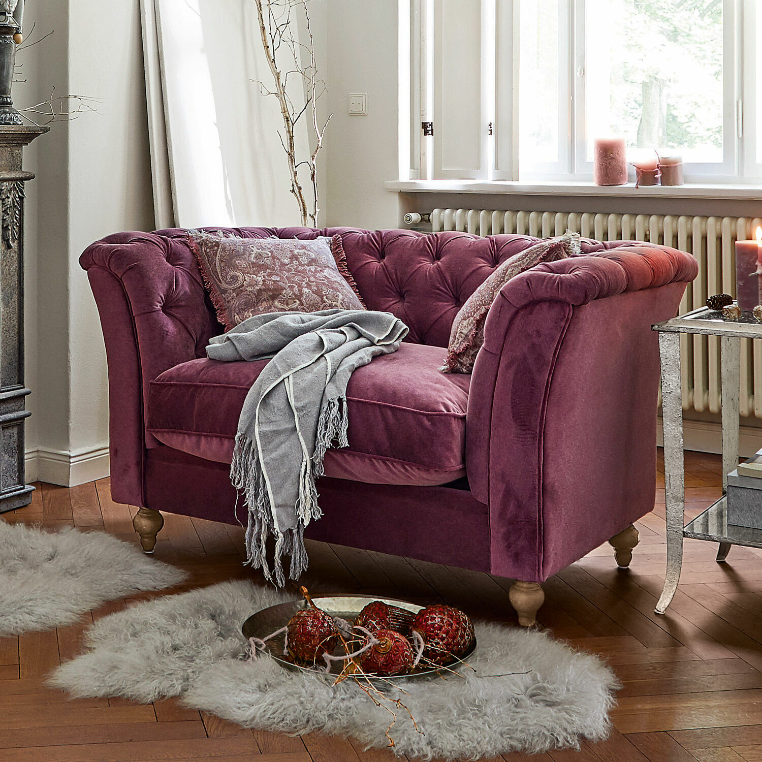 Sofa Clères Zweisitziges Samtsofa in Violett mit Kissen und grauem Plaid in gemütlichem Wohnzimmer