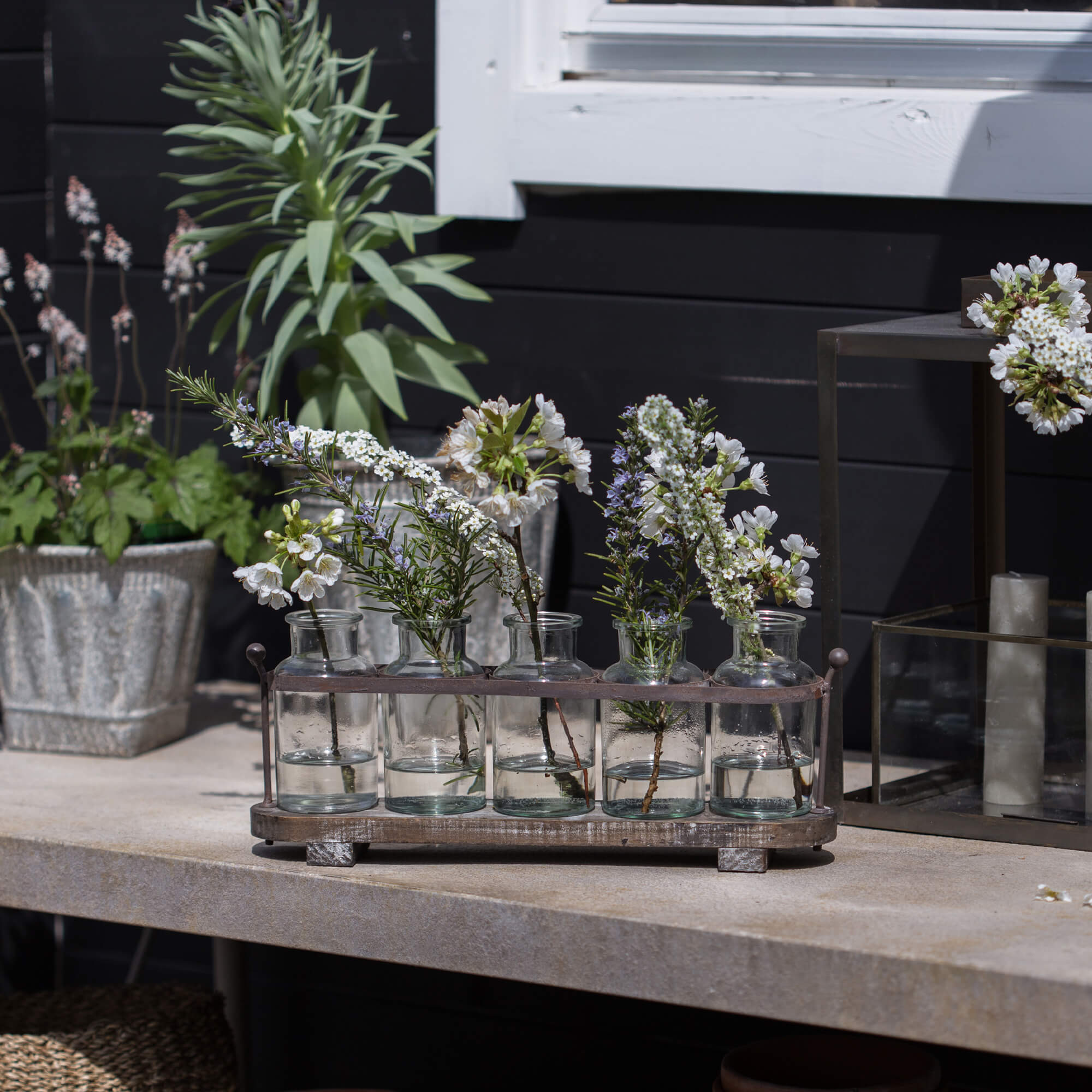 Glasflaschen mit weißen Blumen in Metallhalter auf Steintisch, dekorative Gartendeko