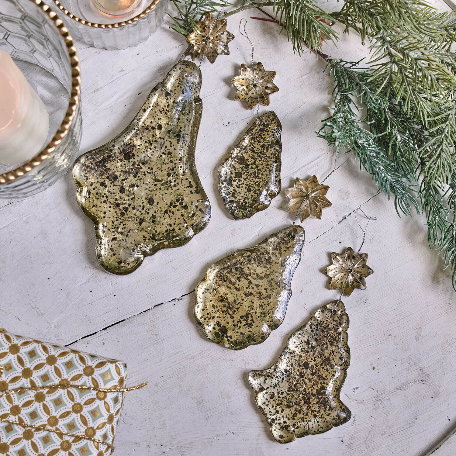 Set aus goldfarbenen Metall-Weihnachtsanhängern in Glocken- und Sternform auf weißem Hintergrund