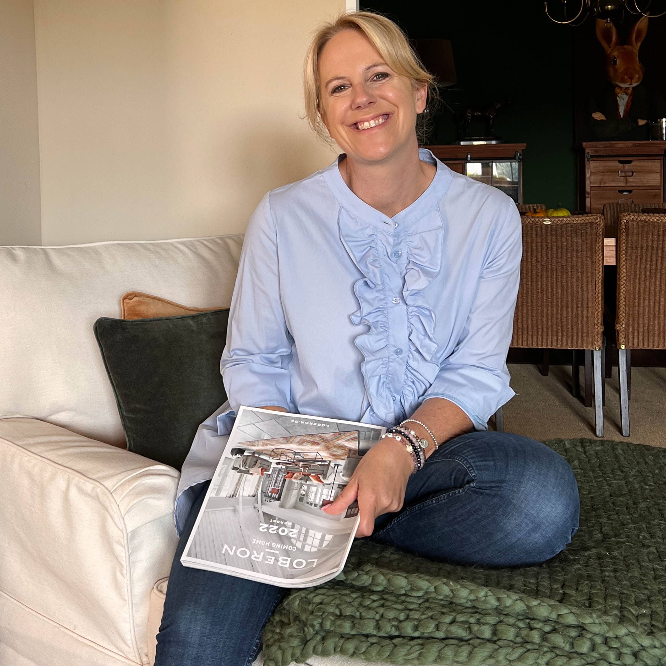 Frau sitzt auf Sofa mit Loberon-Magazin, gemütliches Zuhause mit grünem Strickdecke und Kissen