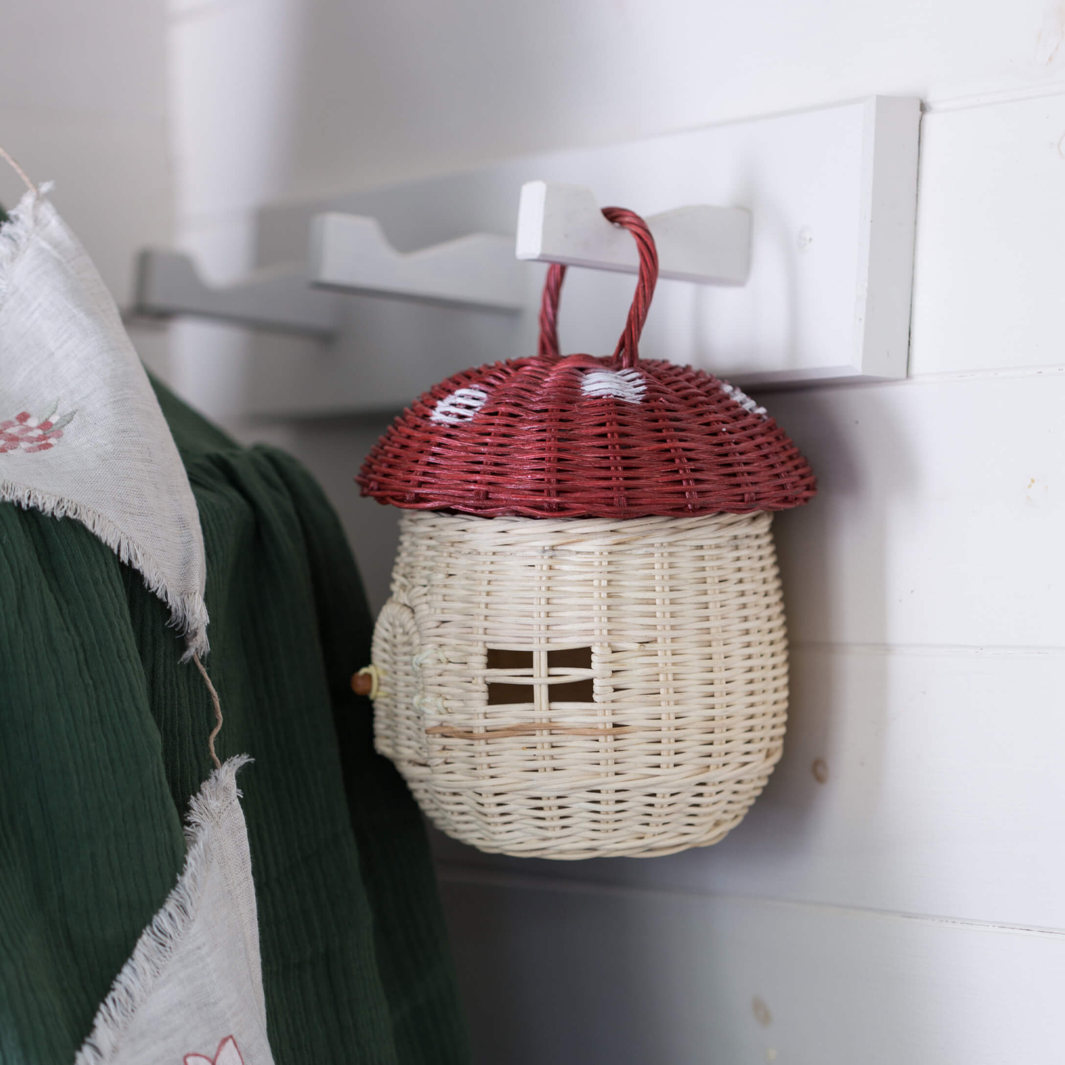 Dekorativer Korb aus Weide in Form eines Fliegenpilzes mit rotem Hut und weißem Stiel, hängend an Haken