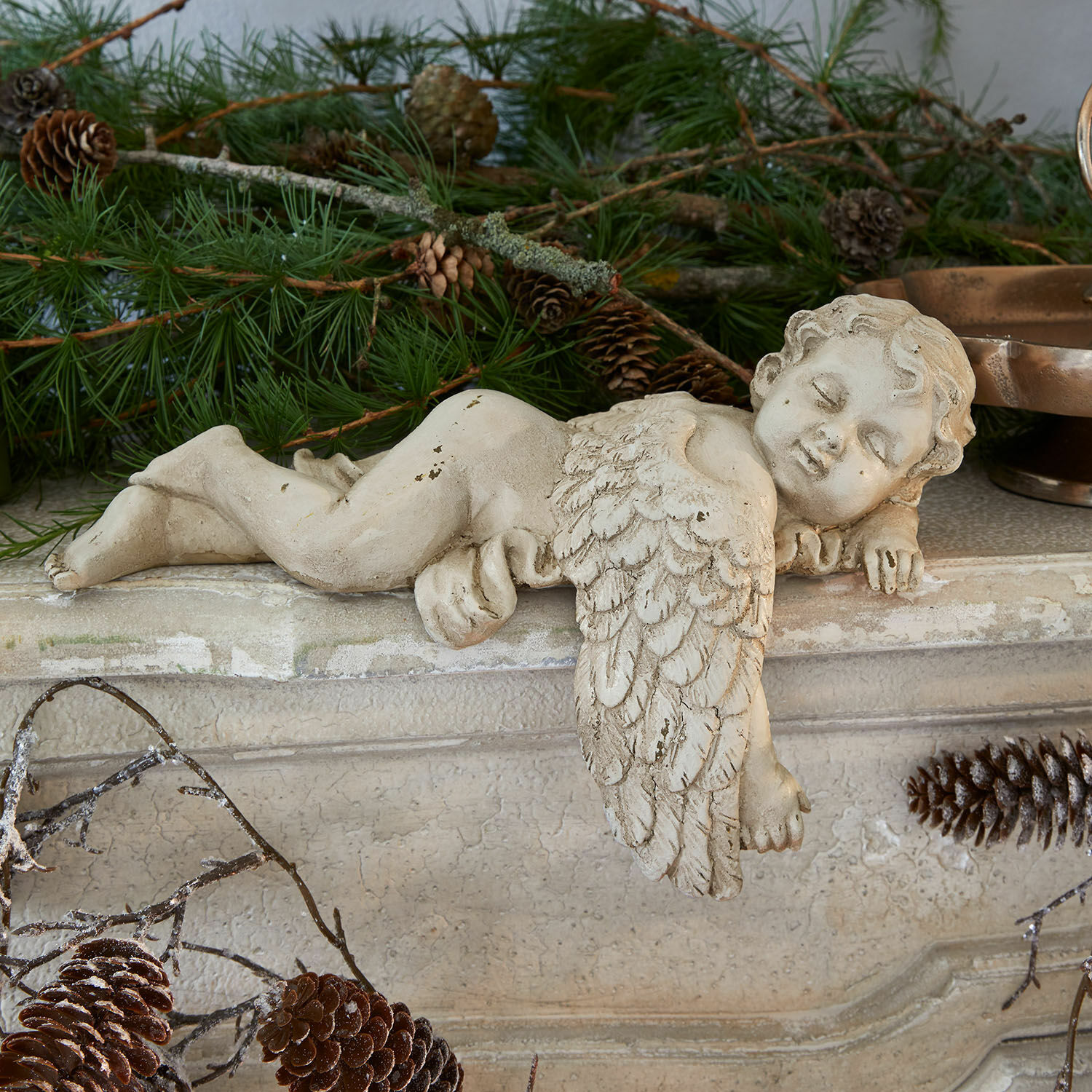 Deko-Engel Deronza Betonfigur eines cremefarbenen Engels auf Kaminsims mit Tannenzweigen und Zapfen, Weihnachtsdeko