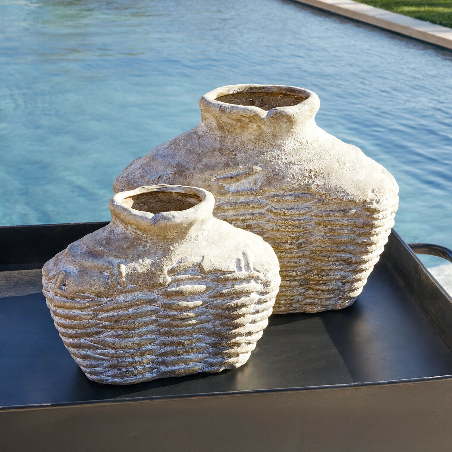 Vase 2er Set Orlaithea Zwei dekorative beige Steinvase auf schwarzem Tablett neben einem Pool